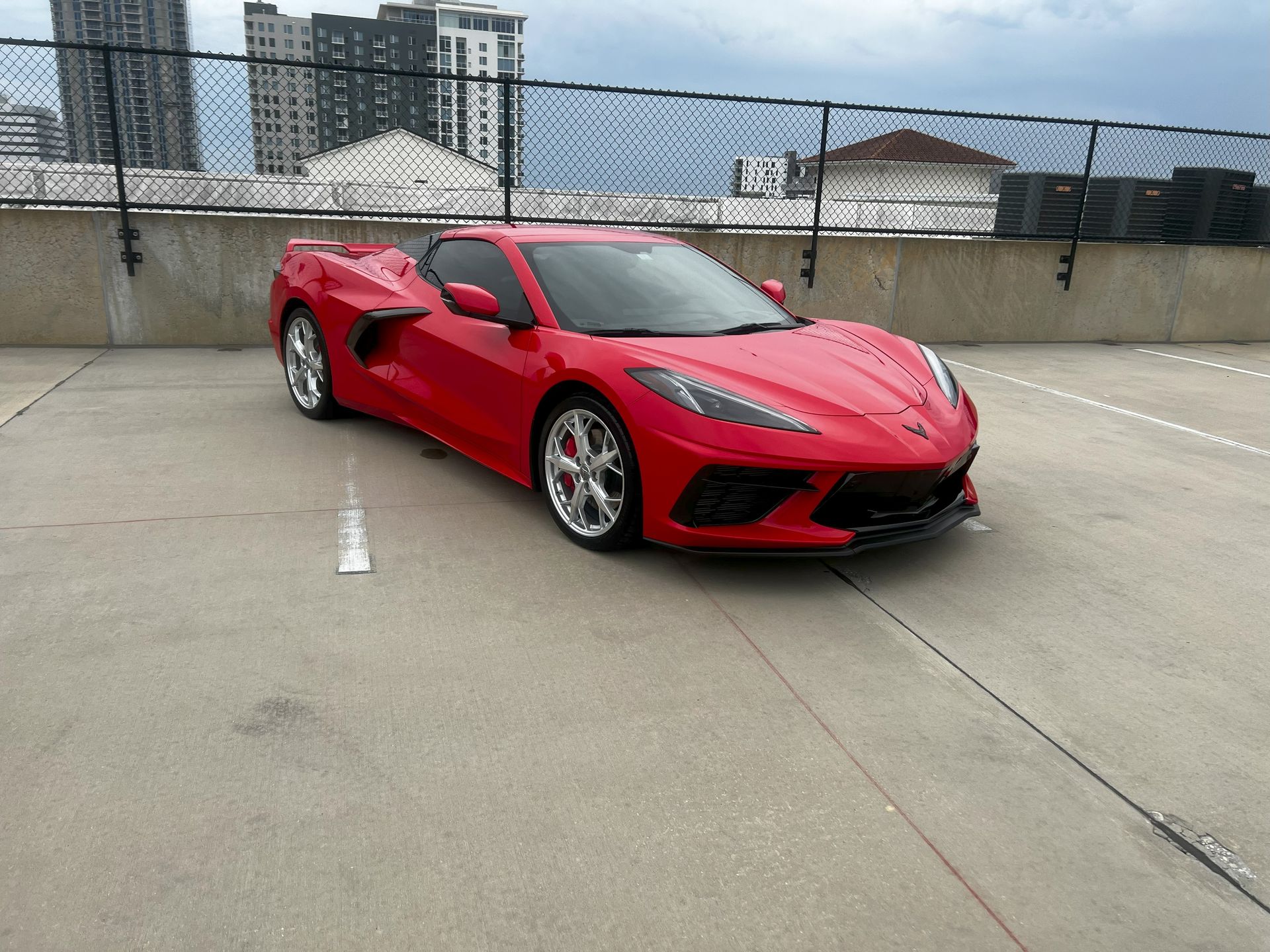 Red sports car parked on a rooftop parking lot. City buildings in the background.