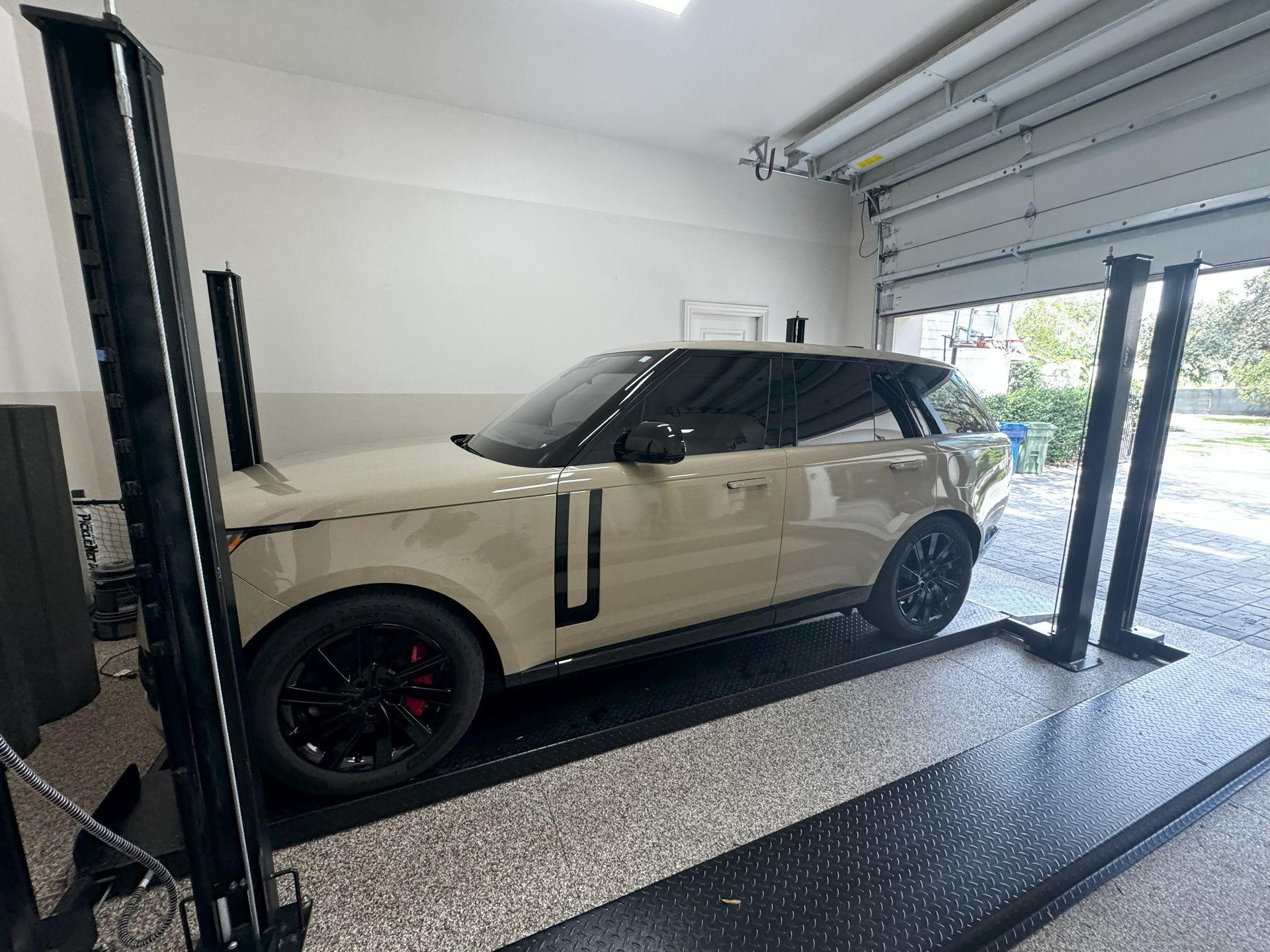 Tan Range Rover on a black car lift inside a garage with the door open.