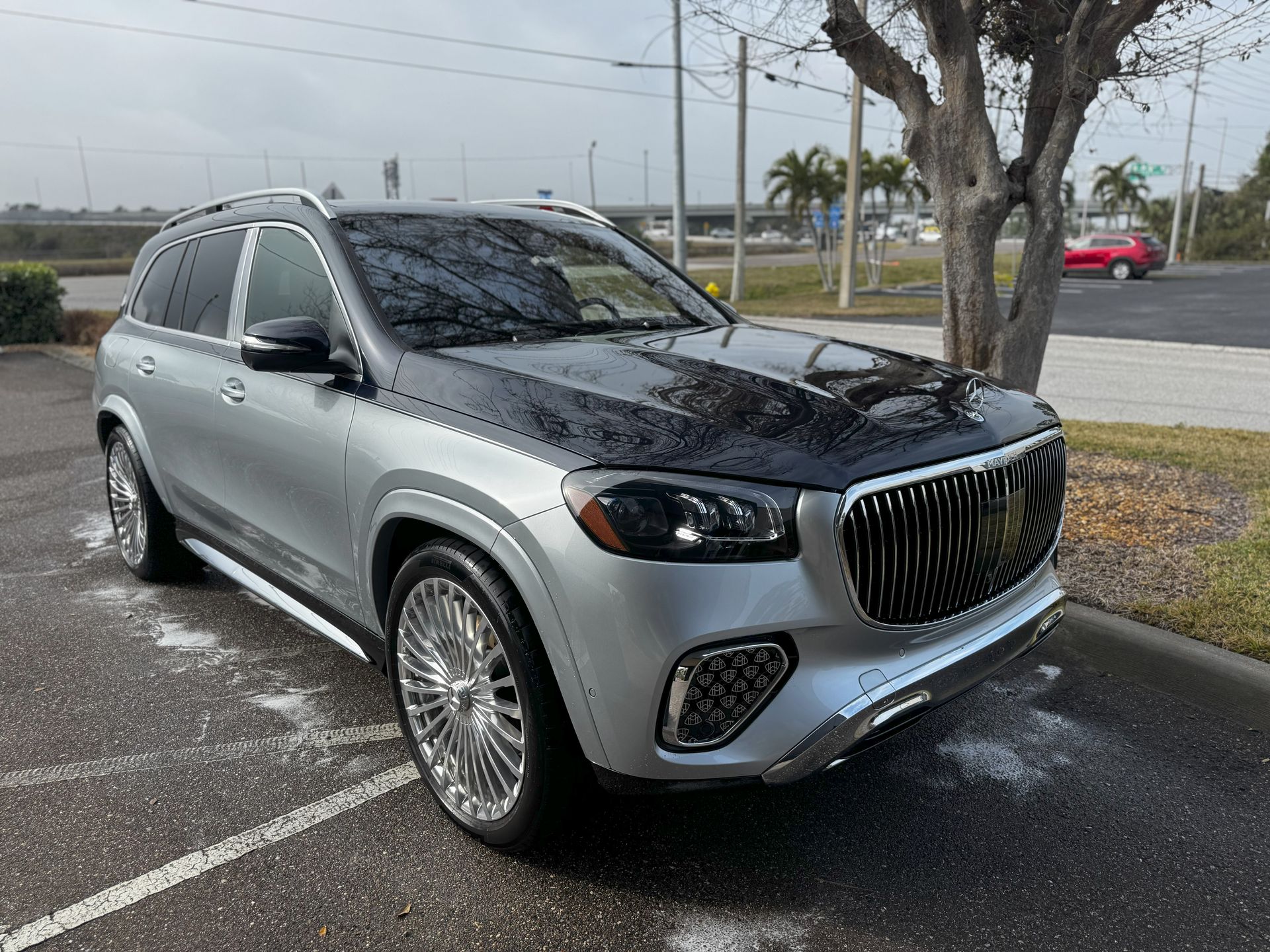 Silver and black Mercedes-Maybach GLS SUV parked on a paved lot. Chrome wheels and grill.
