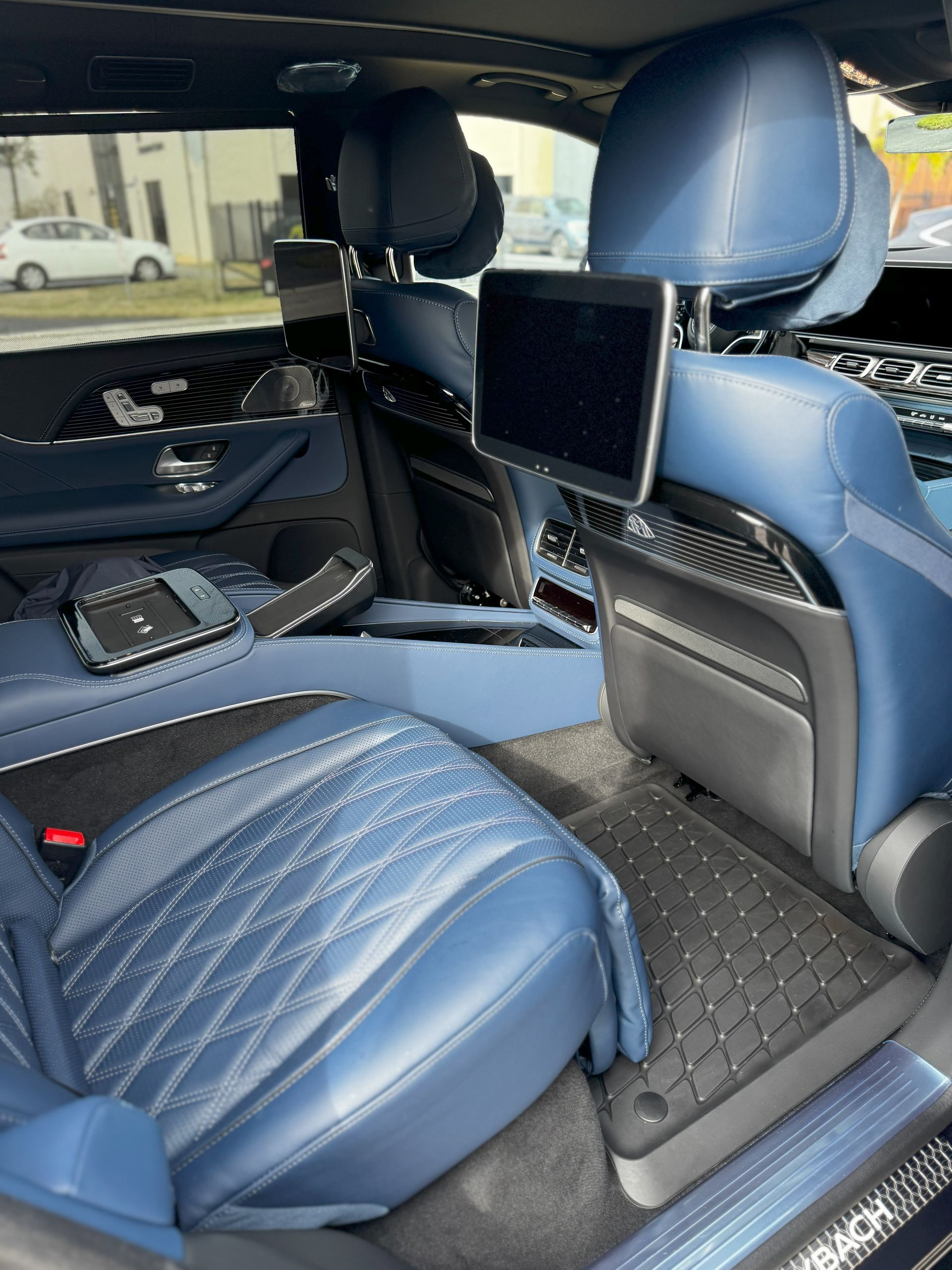 Blue leather interior of a luxury car with backseat screens and diamond stitching.