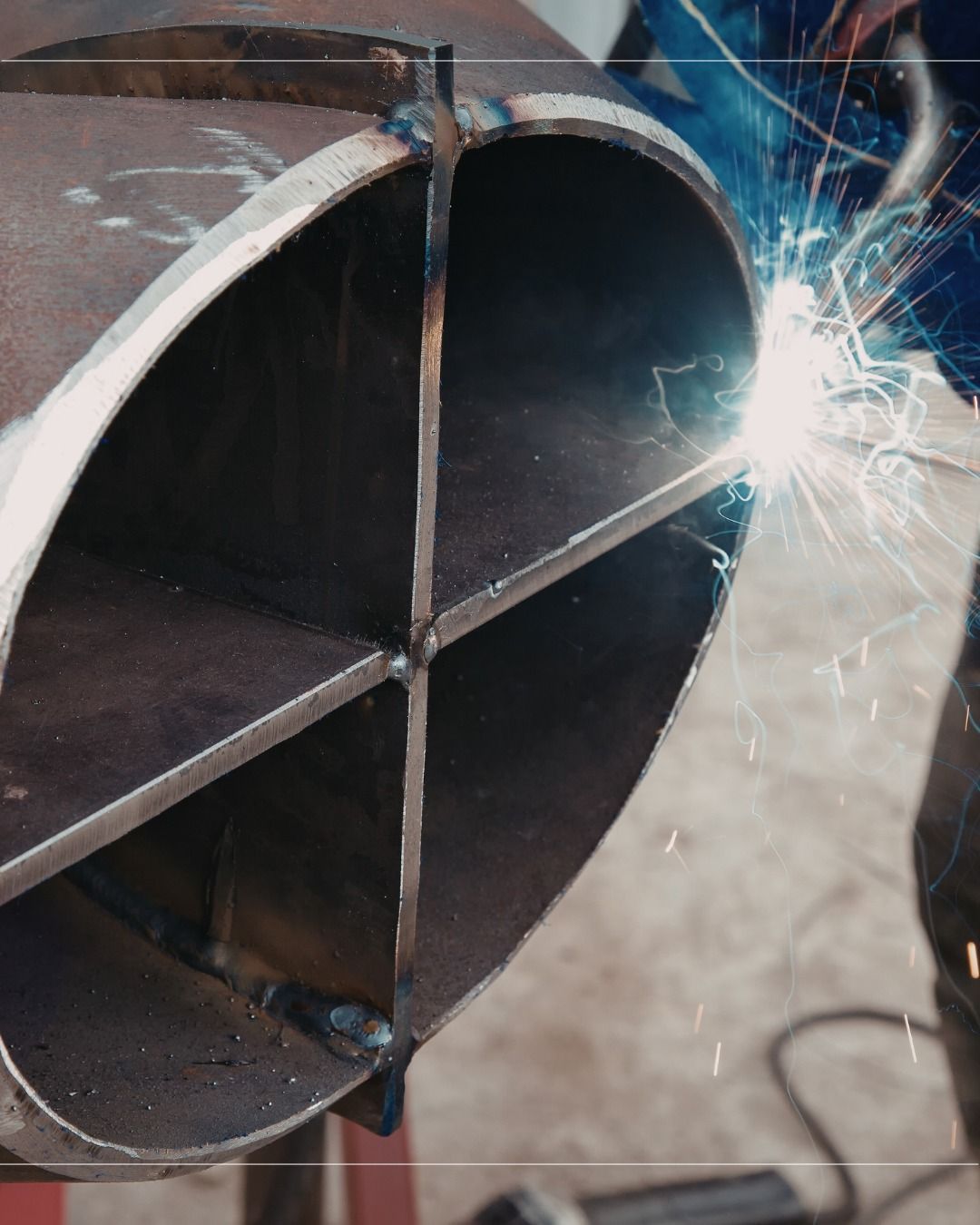 A welder creates sparks while joining metal plates into a four-section divider inside a large steel pipe.