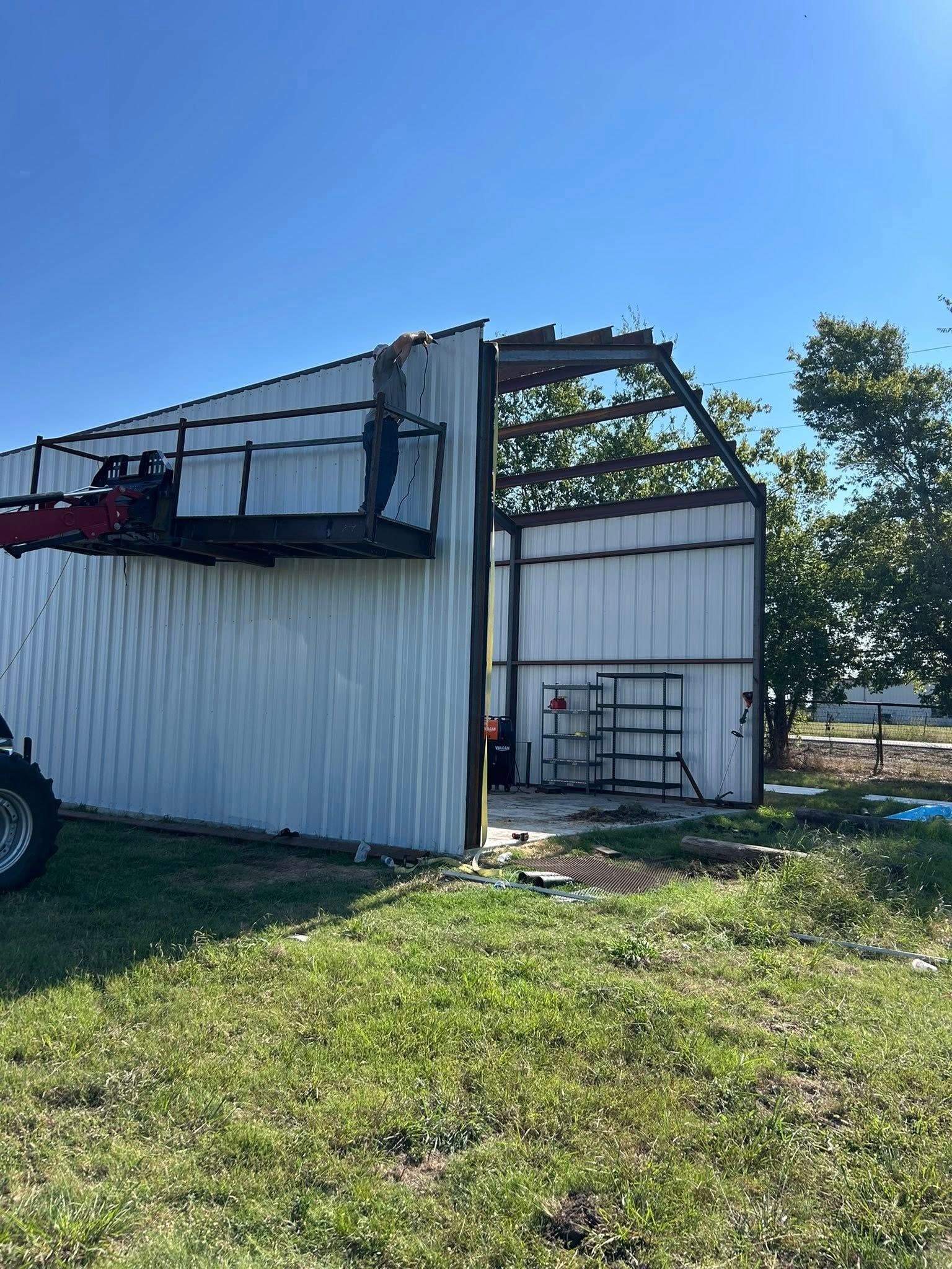 A partially destroyed metal barn with missing roof panels and a piece of heavy machinery parked in front.