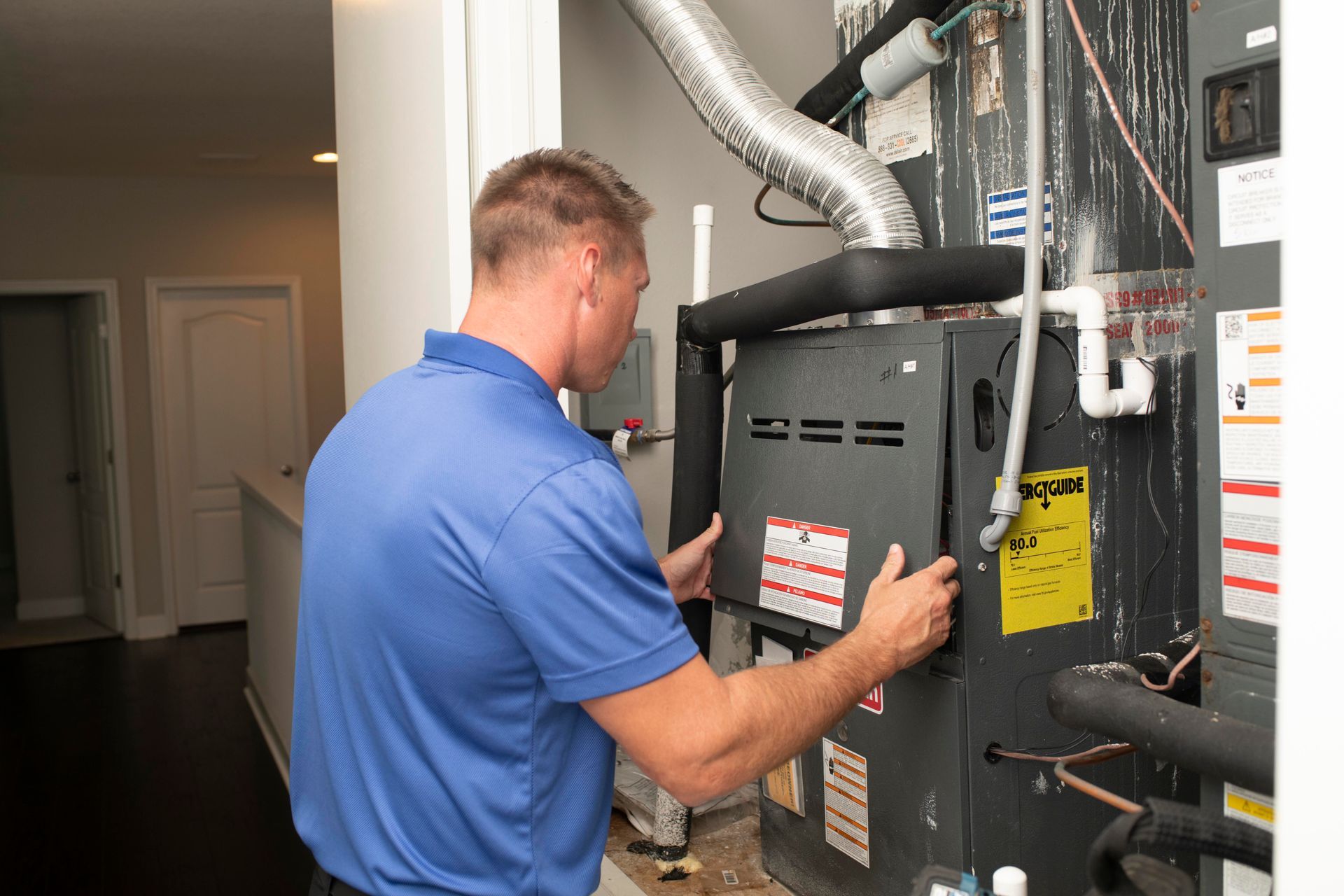 Technician inspecting a furnace unit with exposed ductwork in a utility room