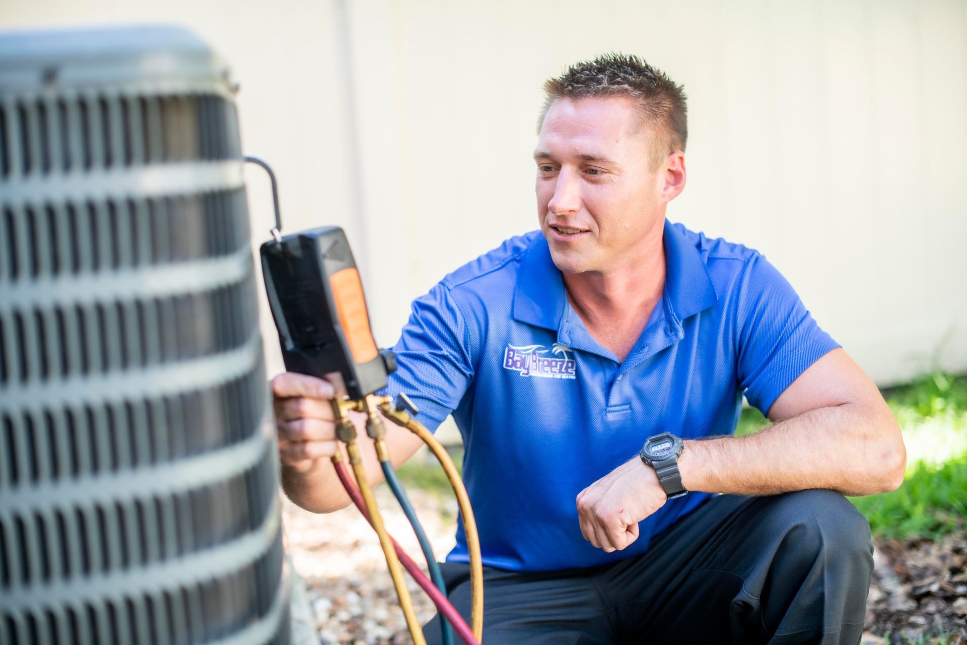 Technician in blue shirt inspecting outdoor HVAC unit with gauges attached