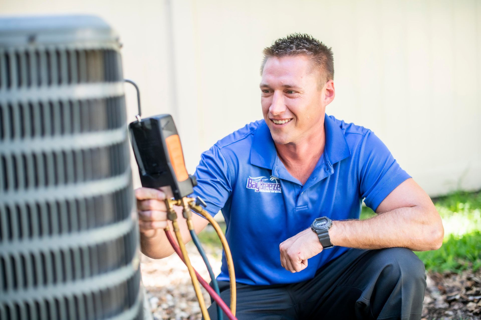 Technician in blue shirt inspecting an outdoor air conditioning unit with a multimeter