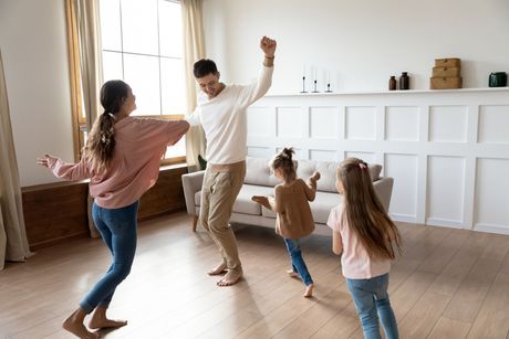 Family dancing in a bright living room, with adults and children moving playfully together.