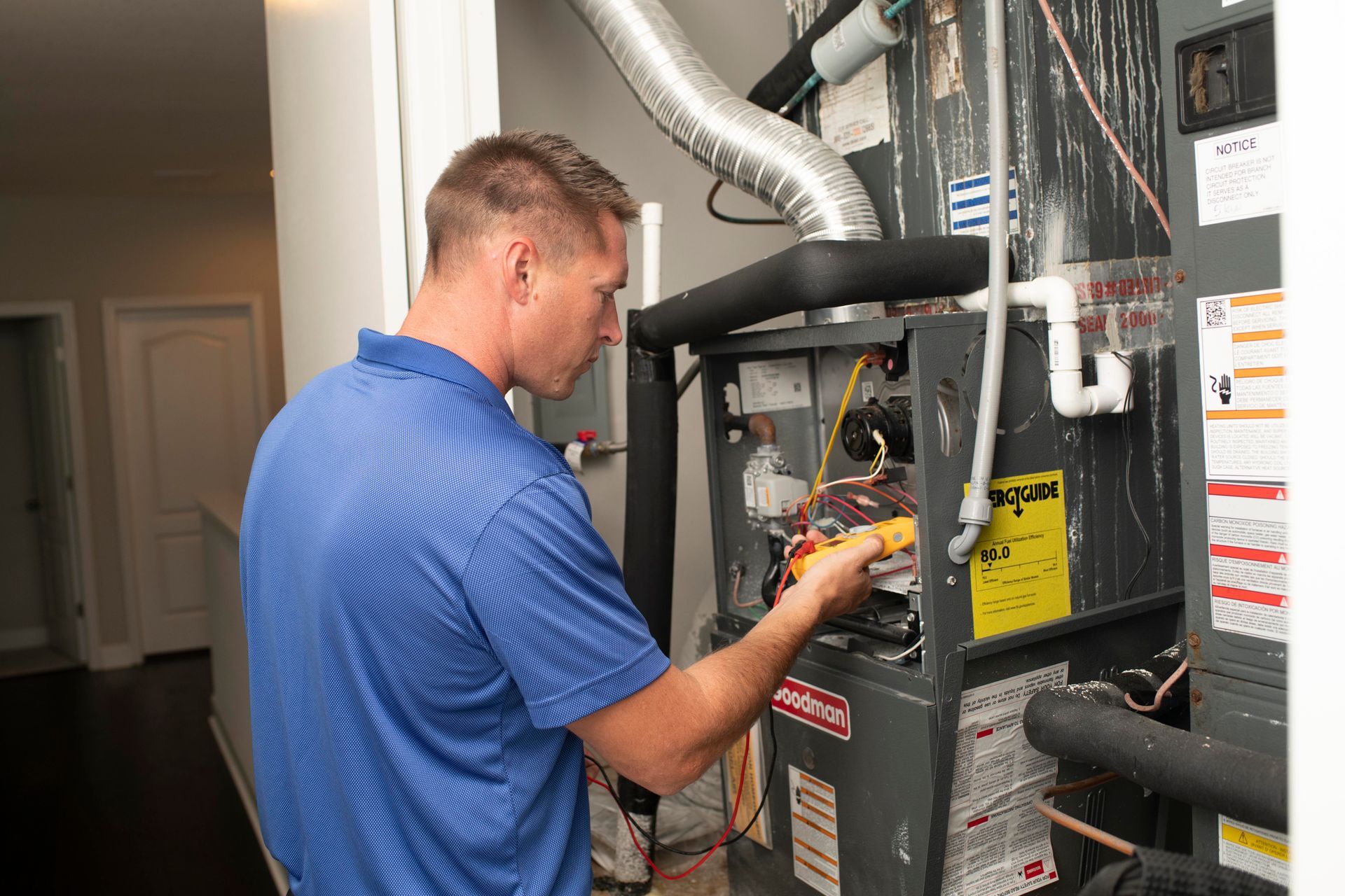 Technician in blue shirt working on a home HVAC unit with tools inside a utility room