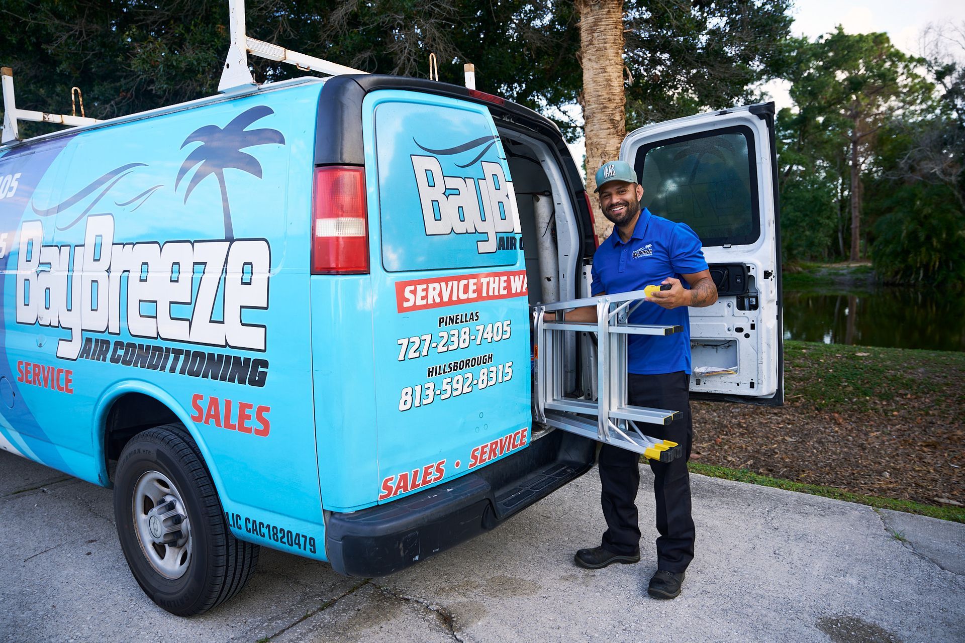 HVAC technician in blue shirt inspecting an outdoor air conditioning unit with gauges attached