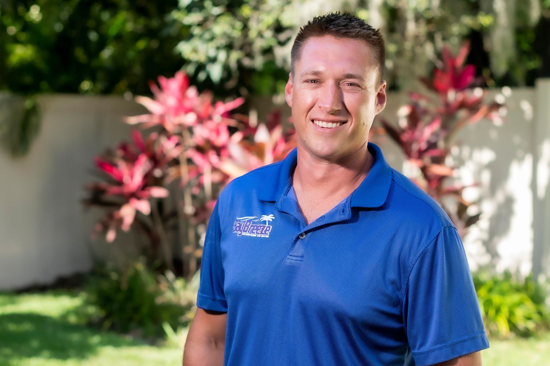 Smiling man in blue polo standing outdoors in a sunny garden.