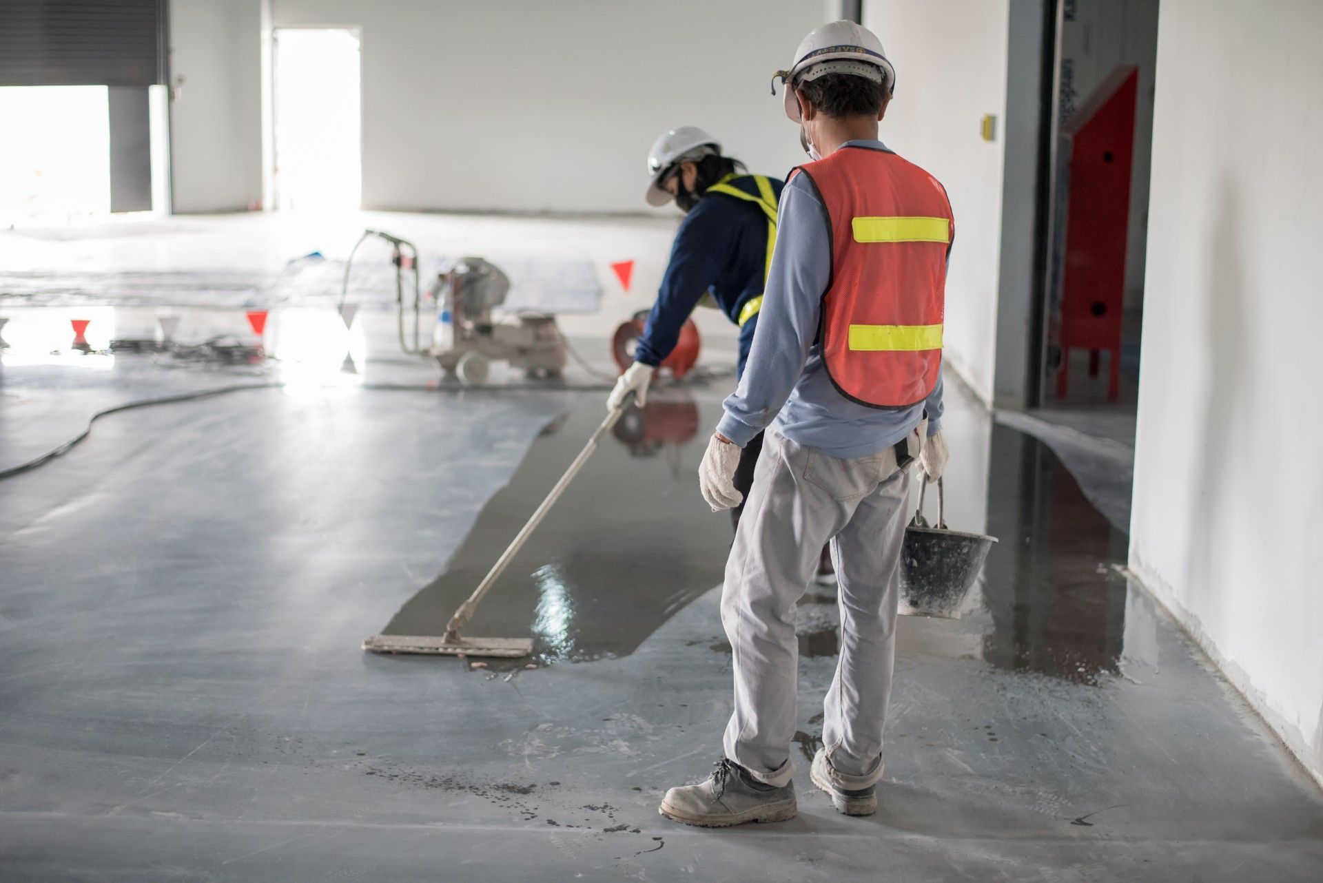 Two construction workers are working on a concrete floor.