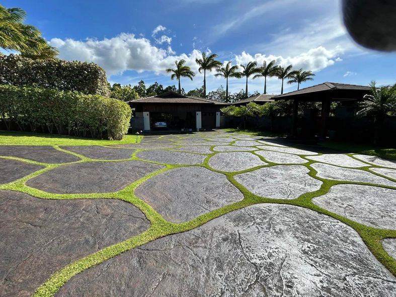 A stone driveway leading to a house with palm trees in the background.