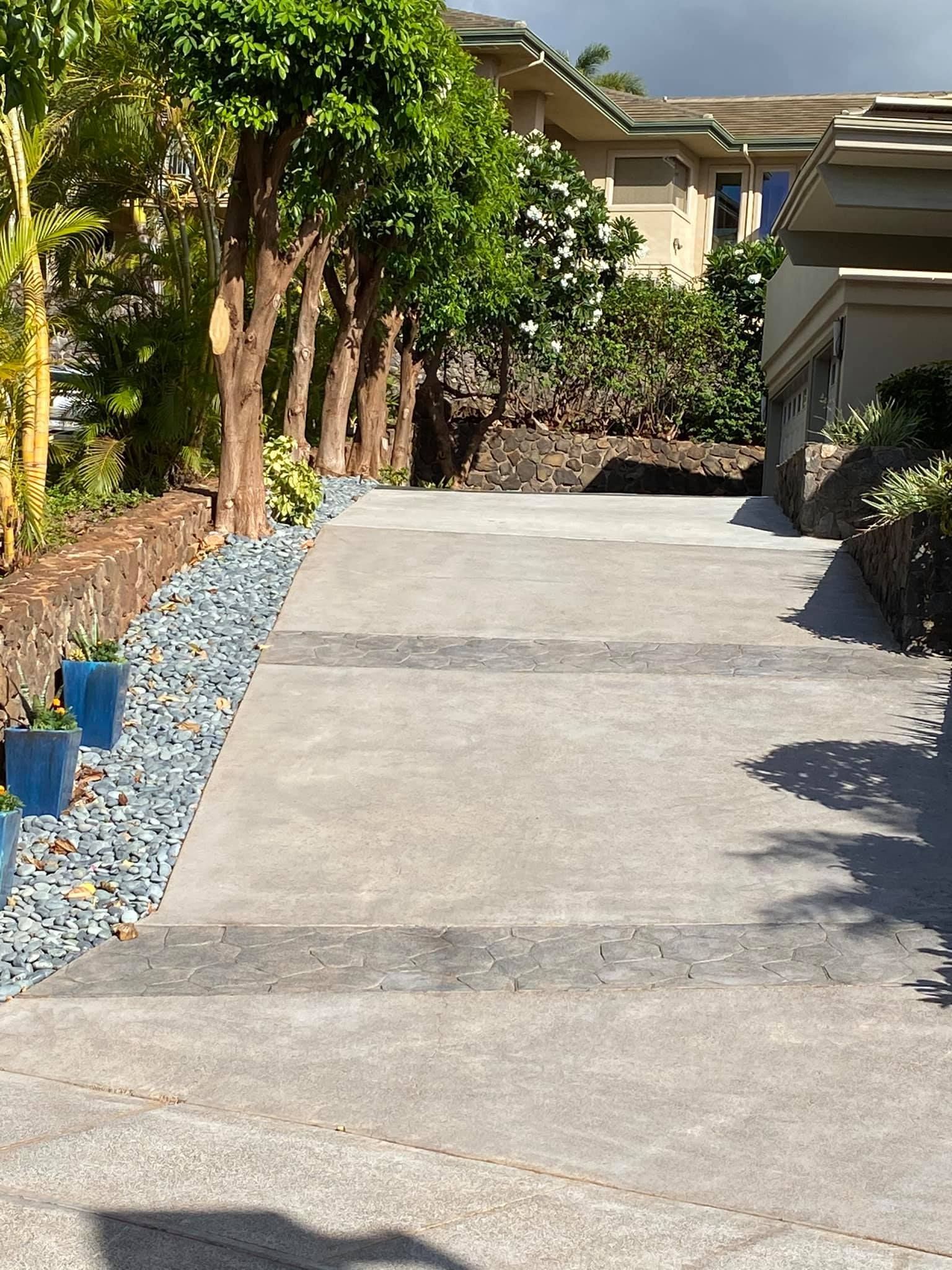 A concrete driveway leading up to a house surrounded by trees and rocks.