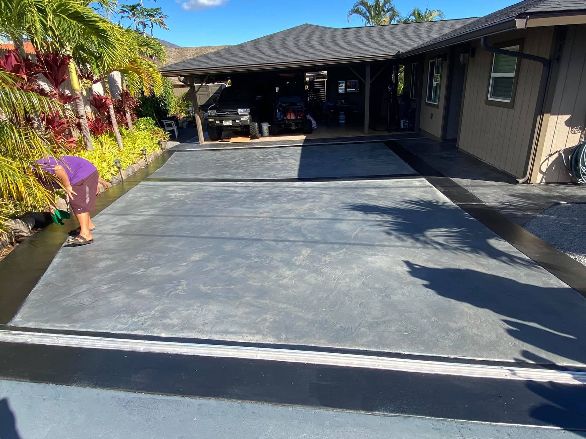 A woman is painting a concrete driveway in front of a house.