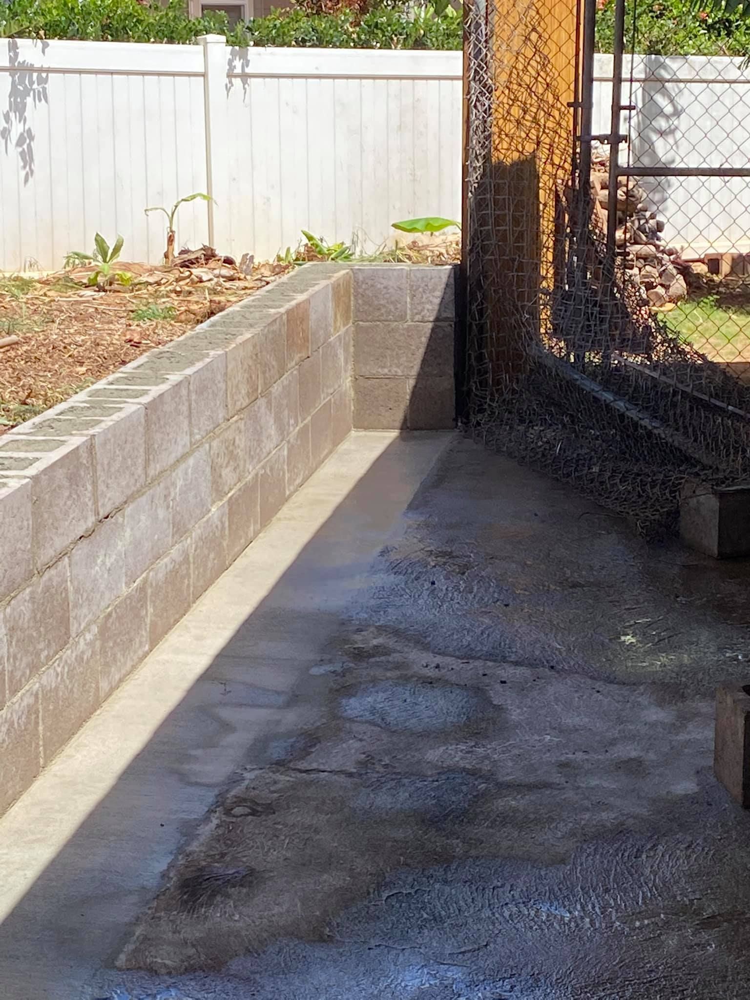 A brick wall is being built in a backyard next to a chain link fence.