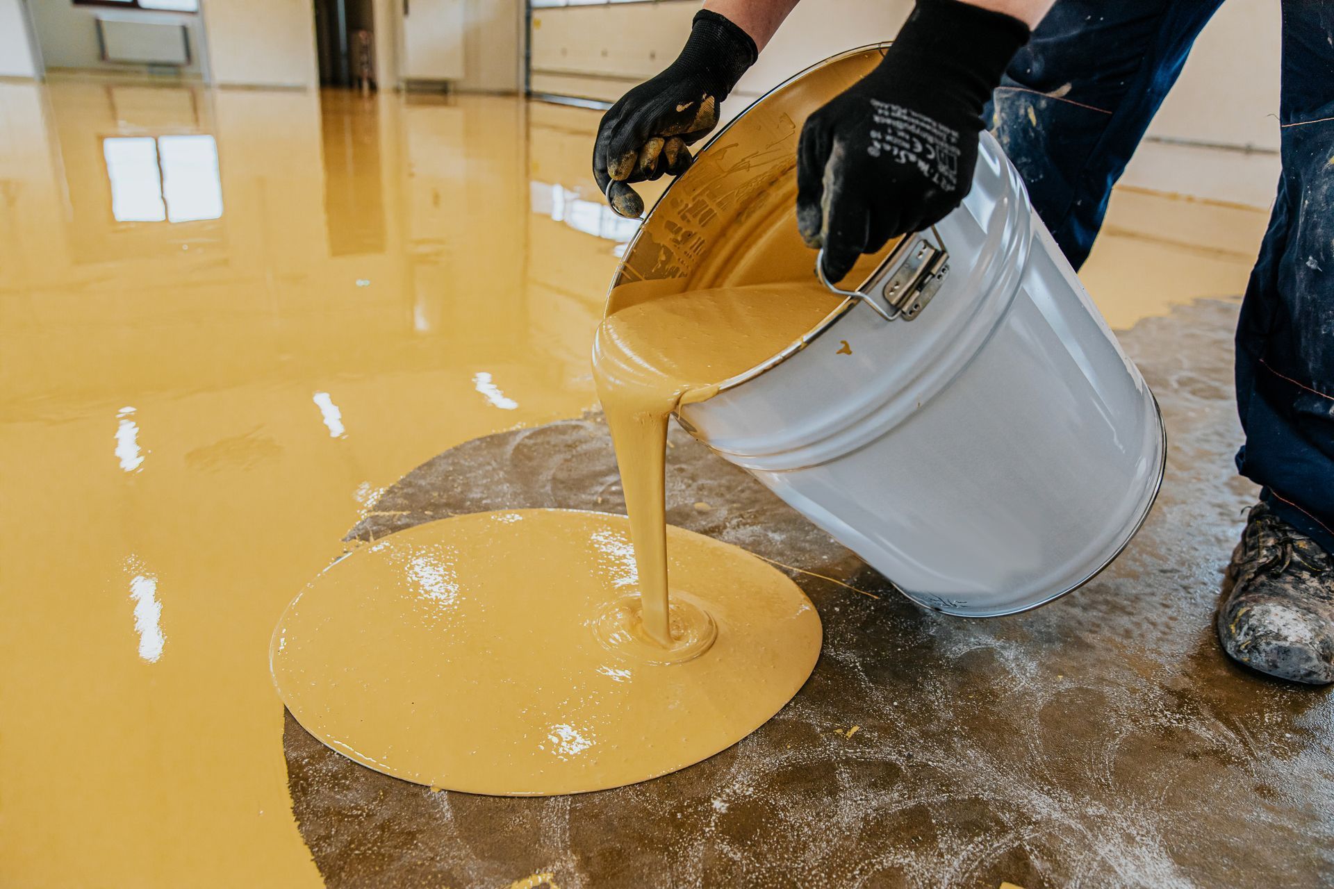 A person is pouring yellow paint into a bucket.