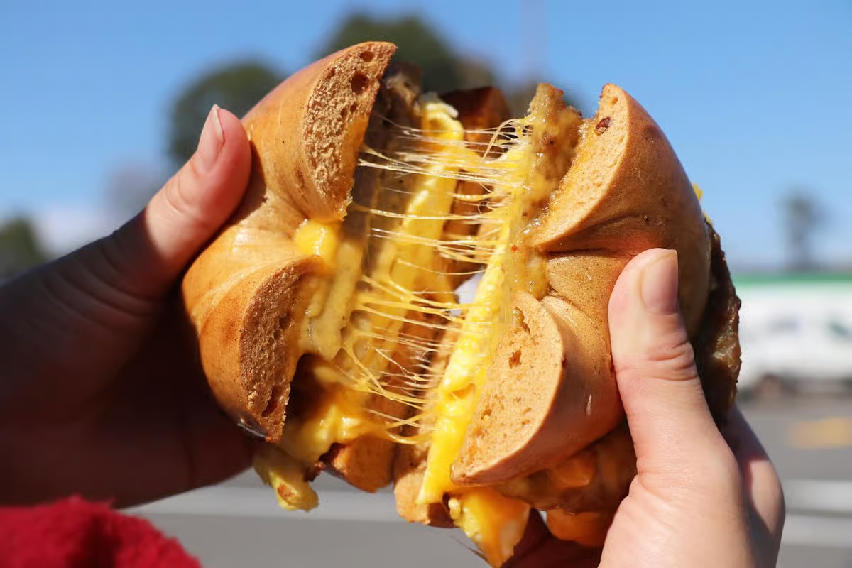 Hands holding a bagel cut open, with melted yellow cheese stretching between the halves.