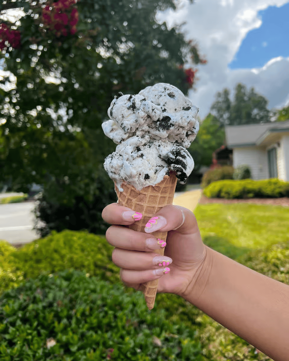 Hand holding a double scoop Oreo ice cream cone outdoors.