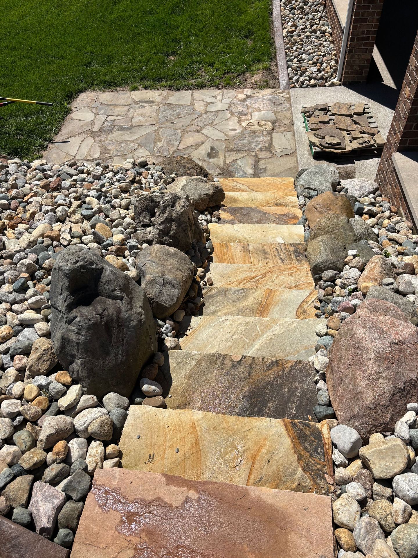 Stone steps through a gravel garden beside a stone wall and green grass.