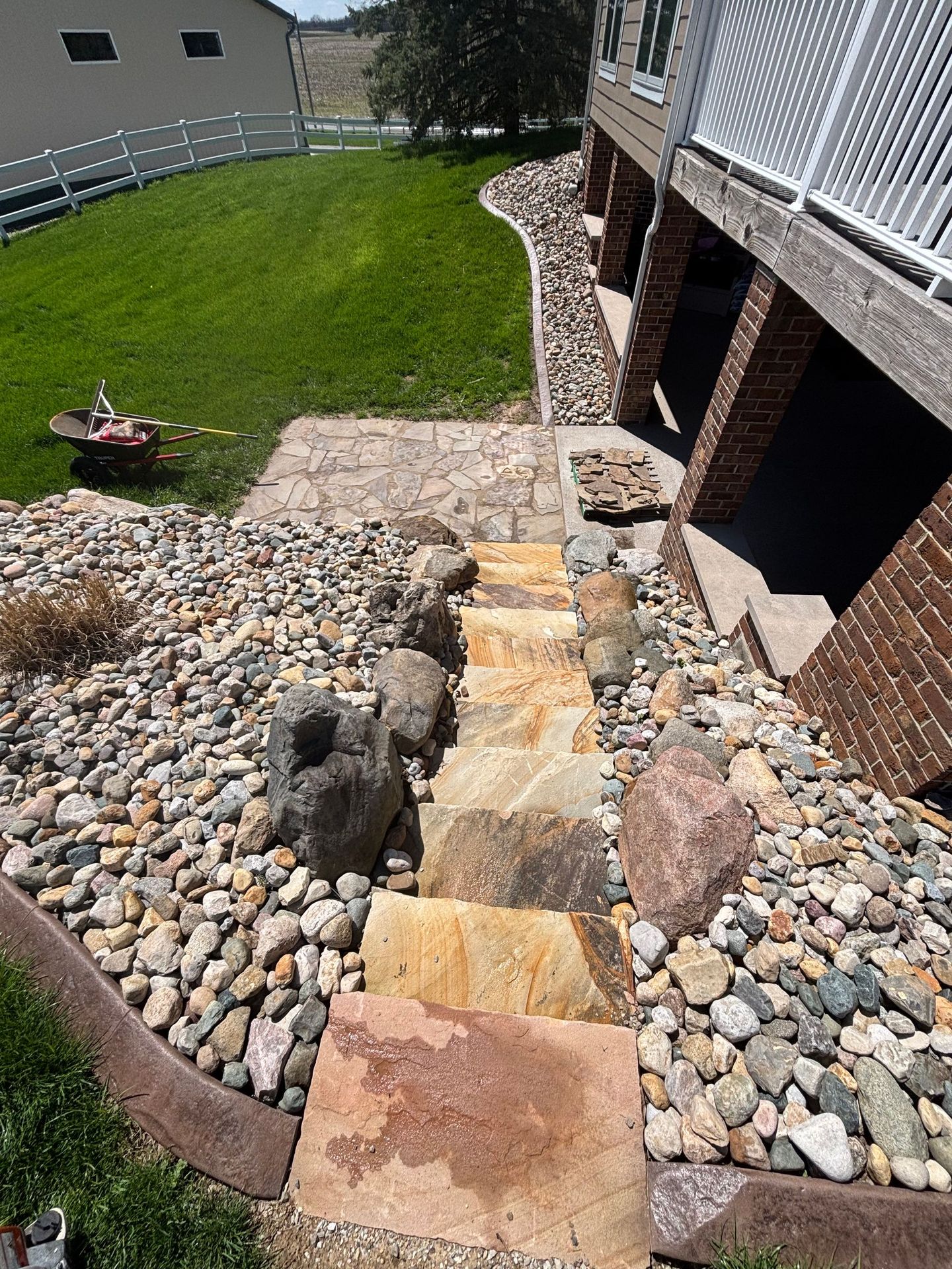 Rocky backyard slope with stone steps leading to a brick house and grassy lawn