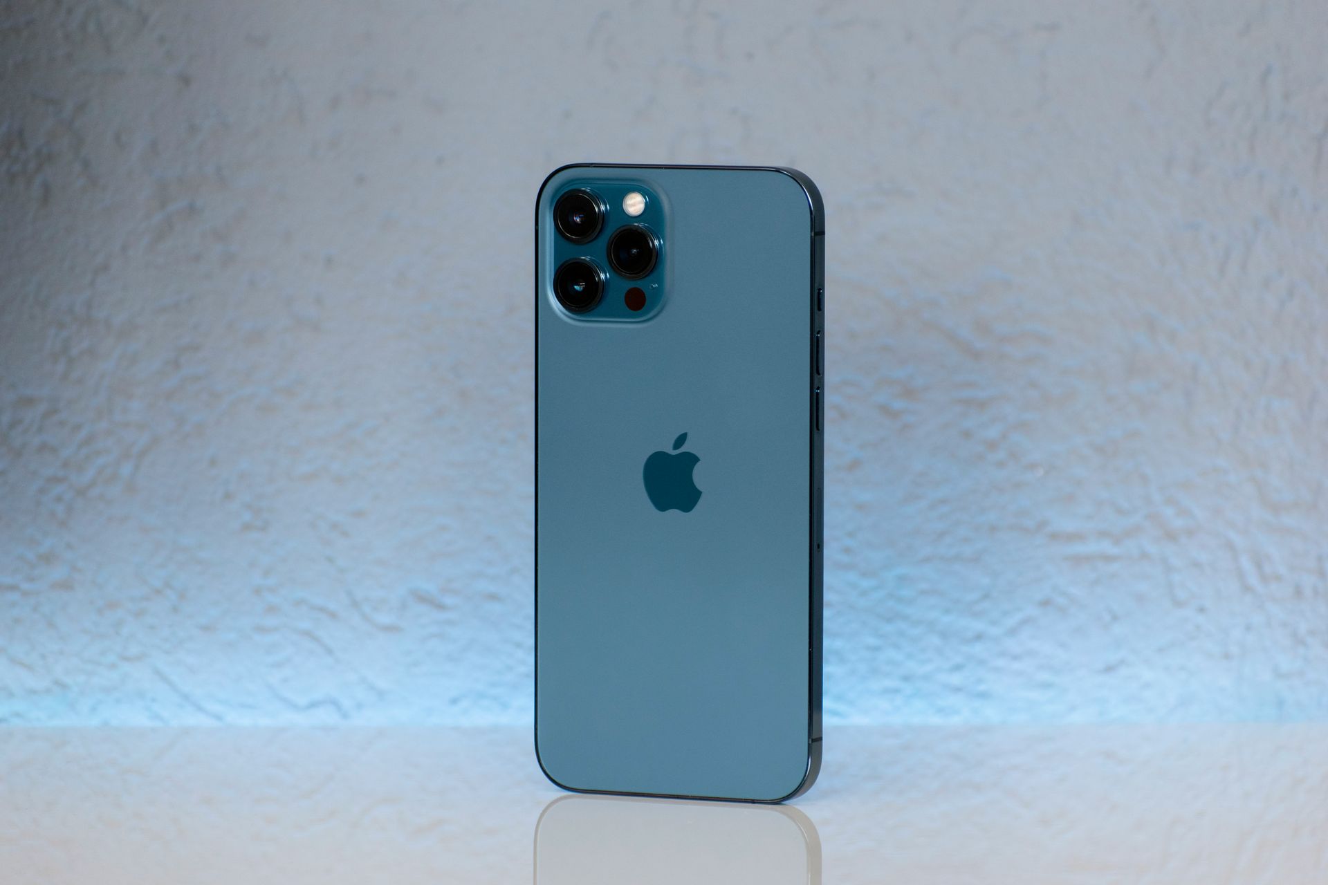 Blue iPhone standing upright on a white surface against a light textured wall