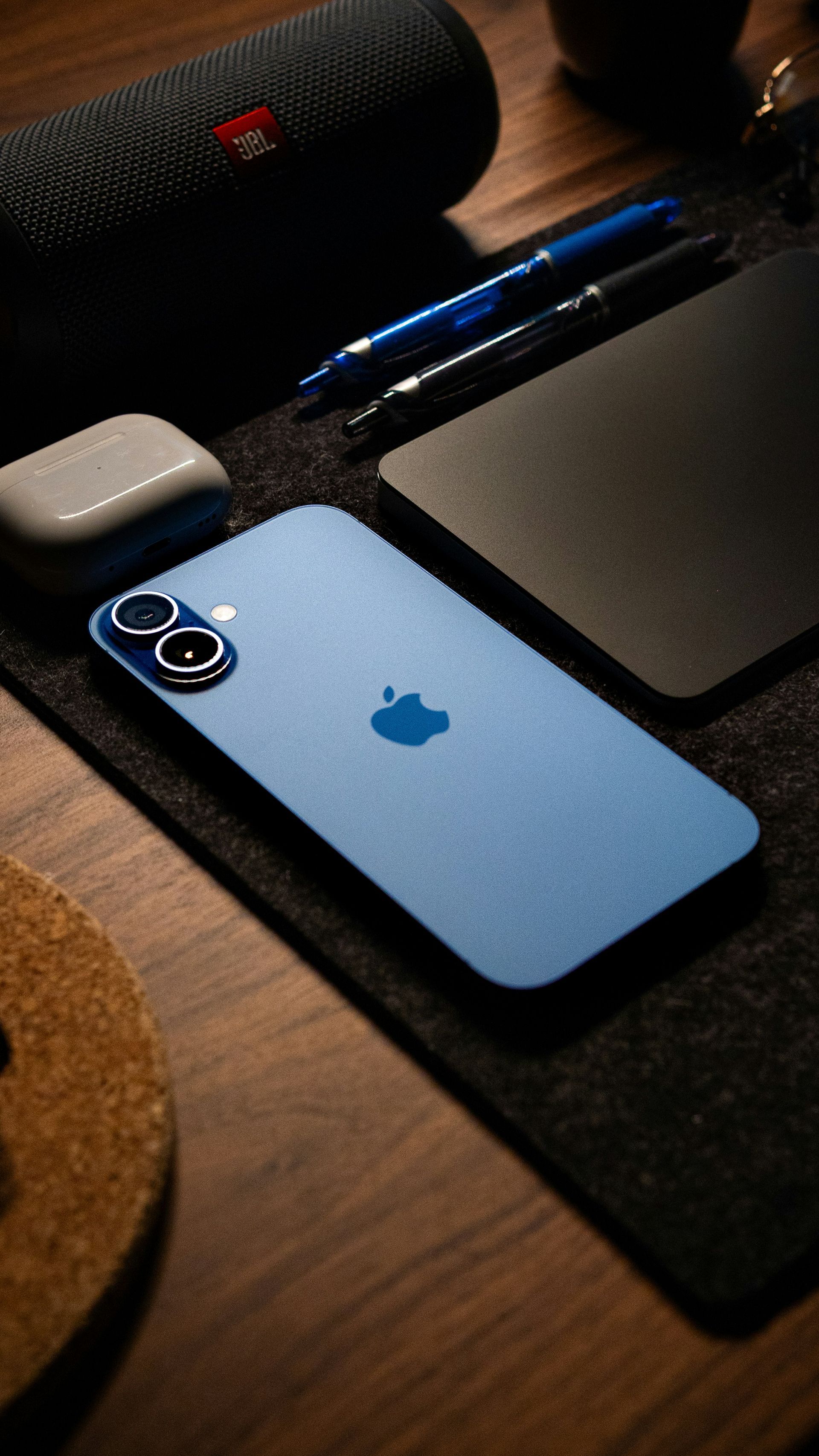 Blue iPhone on a desk beside a black mat, pen, and speaker