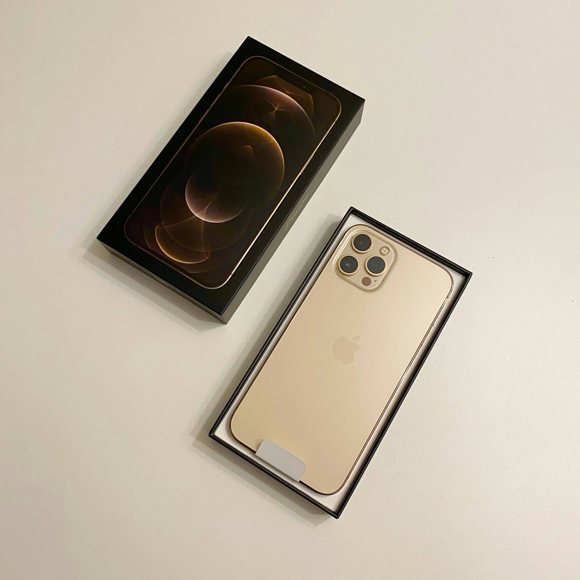 Open smartphone box with a gold phone lying beside its packaging on a light surface