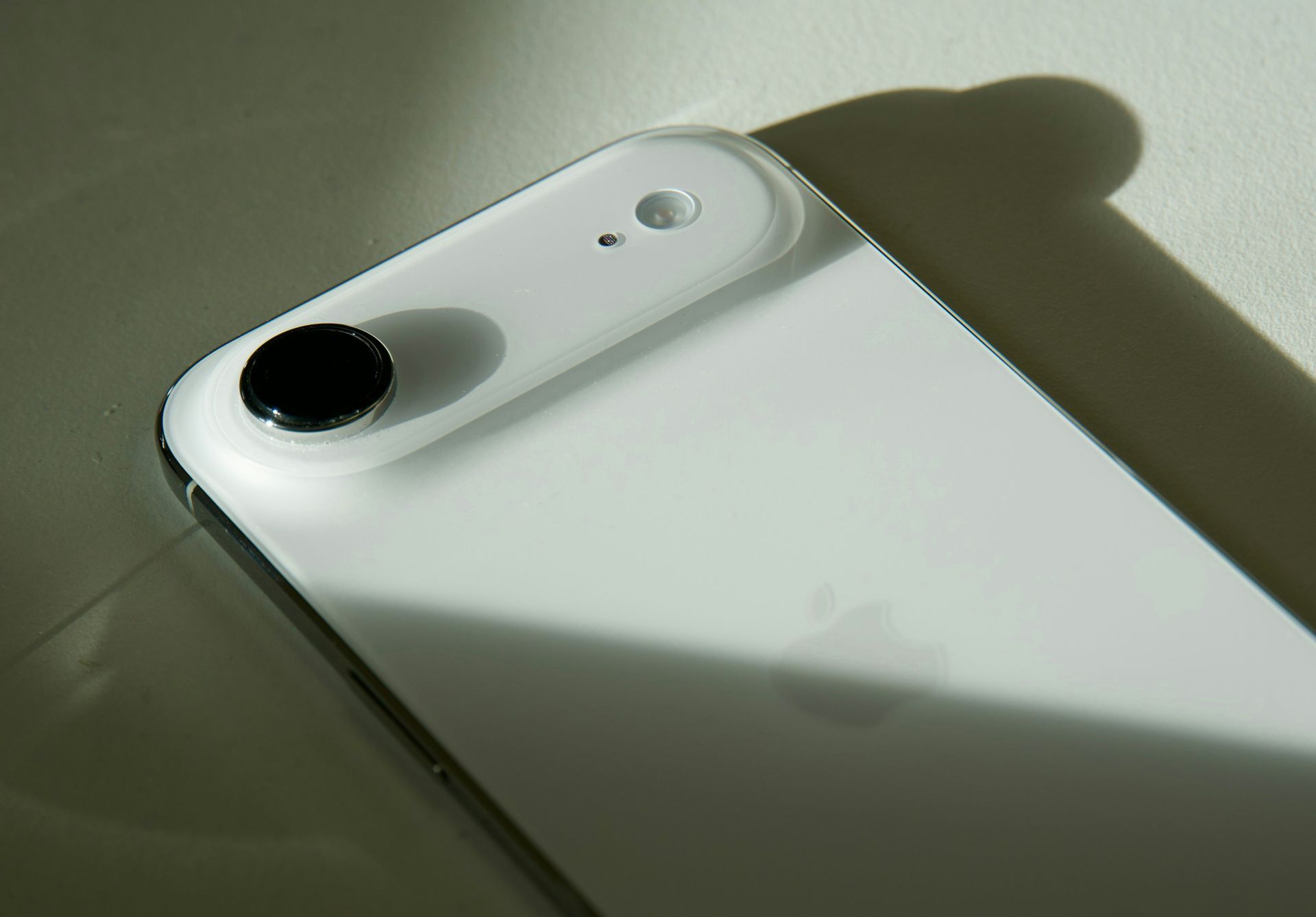 Close-up of a white smartphone with a black camera lens, lit by sunlight and casting a shadow