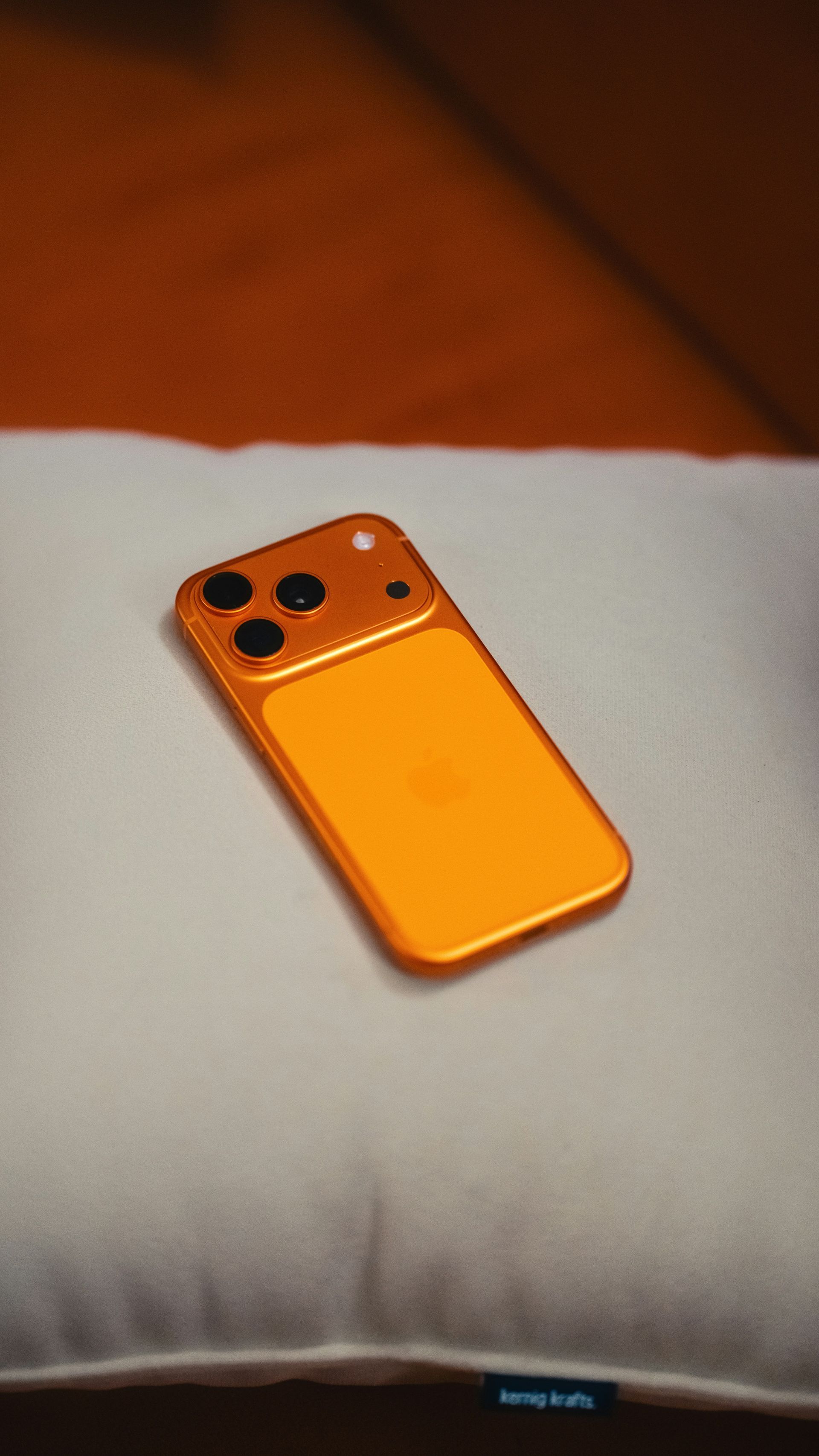 Orange smartphone lying on a white cushion with a brown background