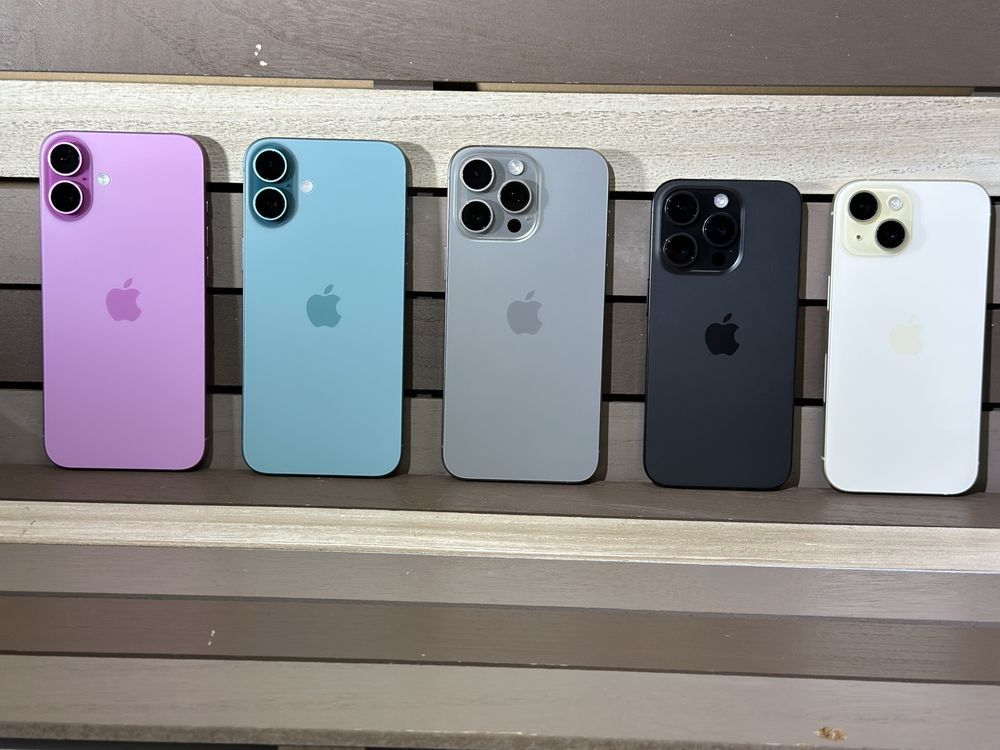 Two iPhones in purple and white rest on a reflective surface in front of their product box displaying the purple model.