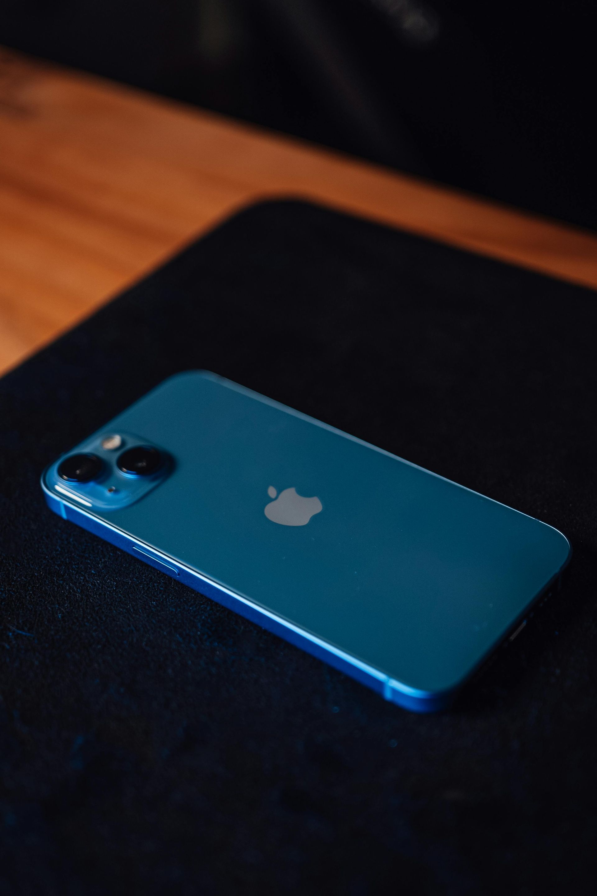 Blue iPhone lying face down on a black surface with a wooden table edge in the background