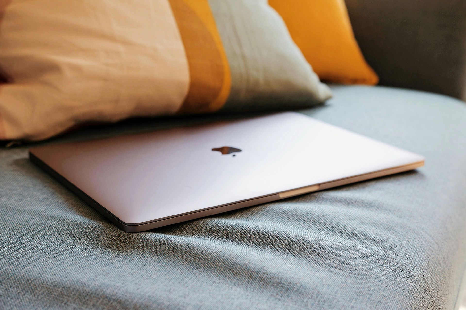 Closed silver laptop on a bed with beige and orange pillows behind it