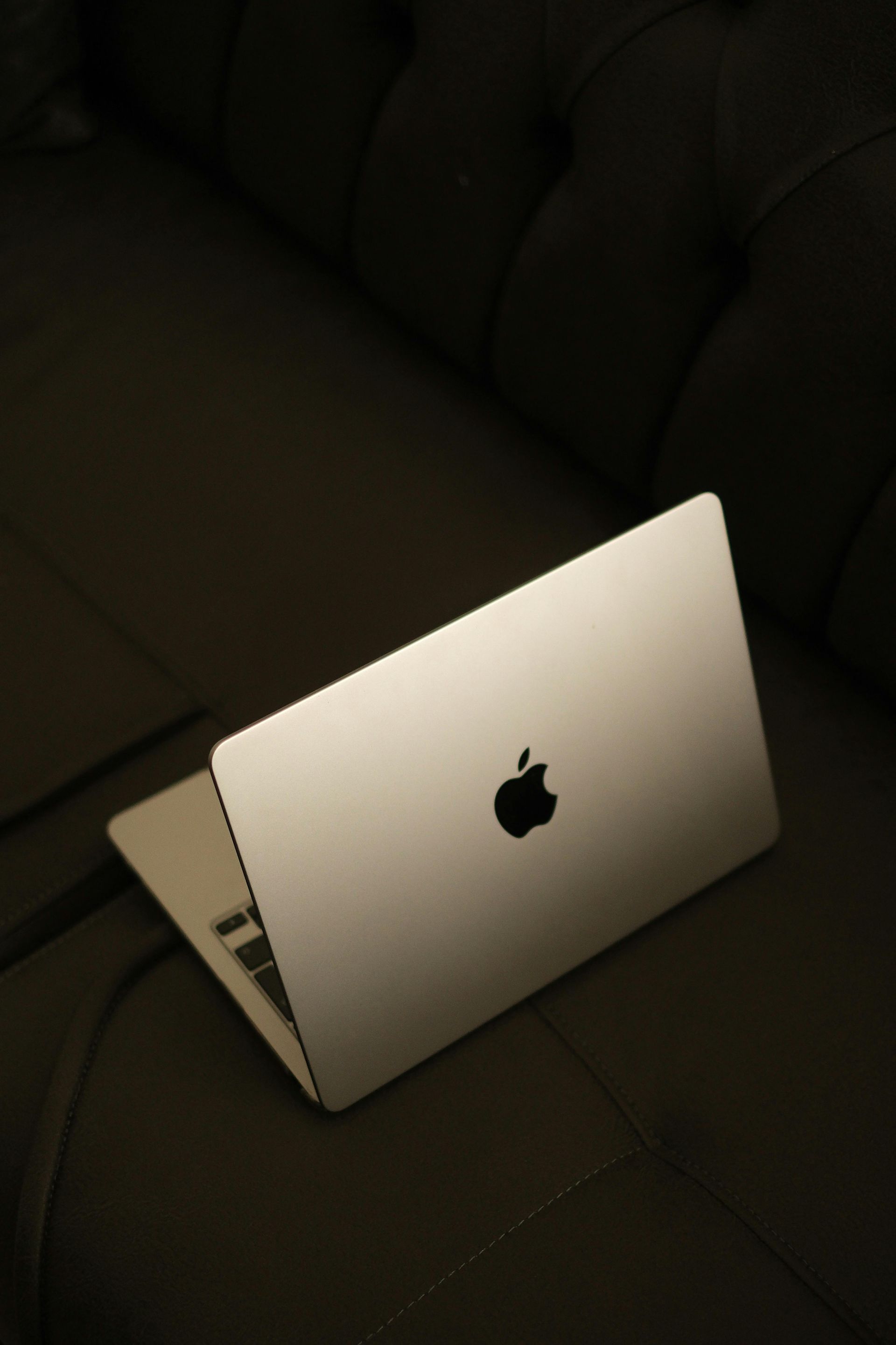 Silver MacBook laptop resting open on a dark couch in dim lighting