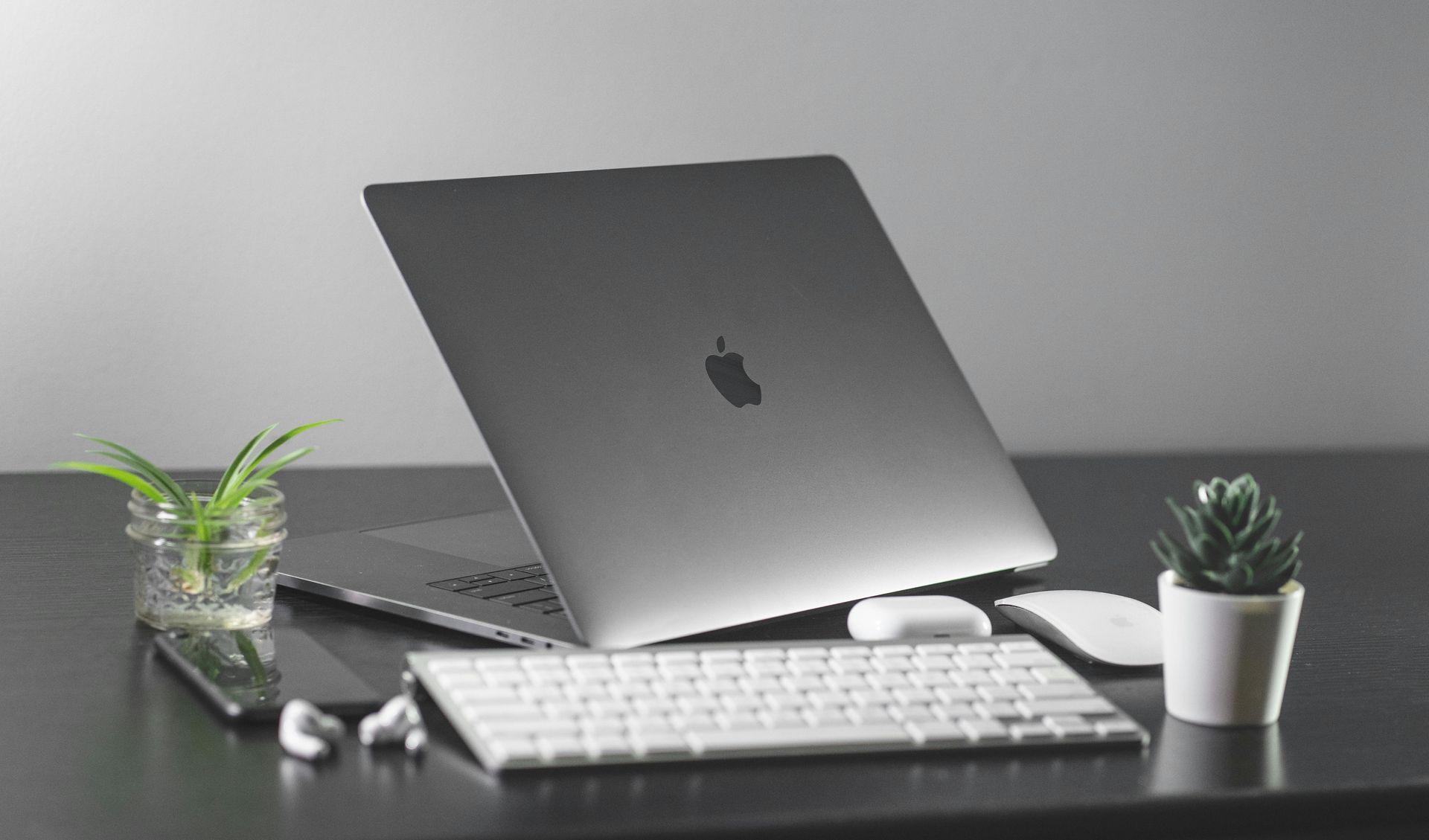 MacBook on a desk with keyboard, mouse, earbuds, and small potted plants