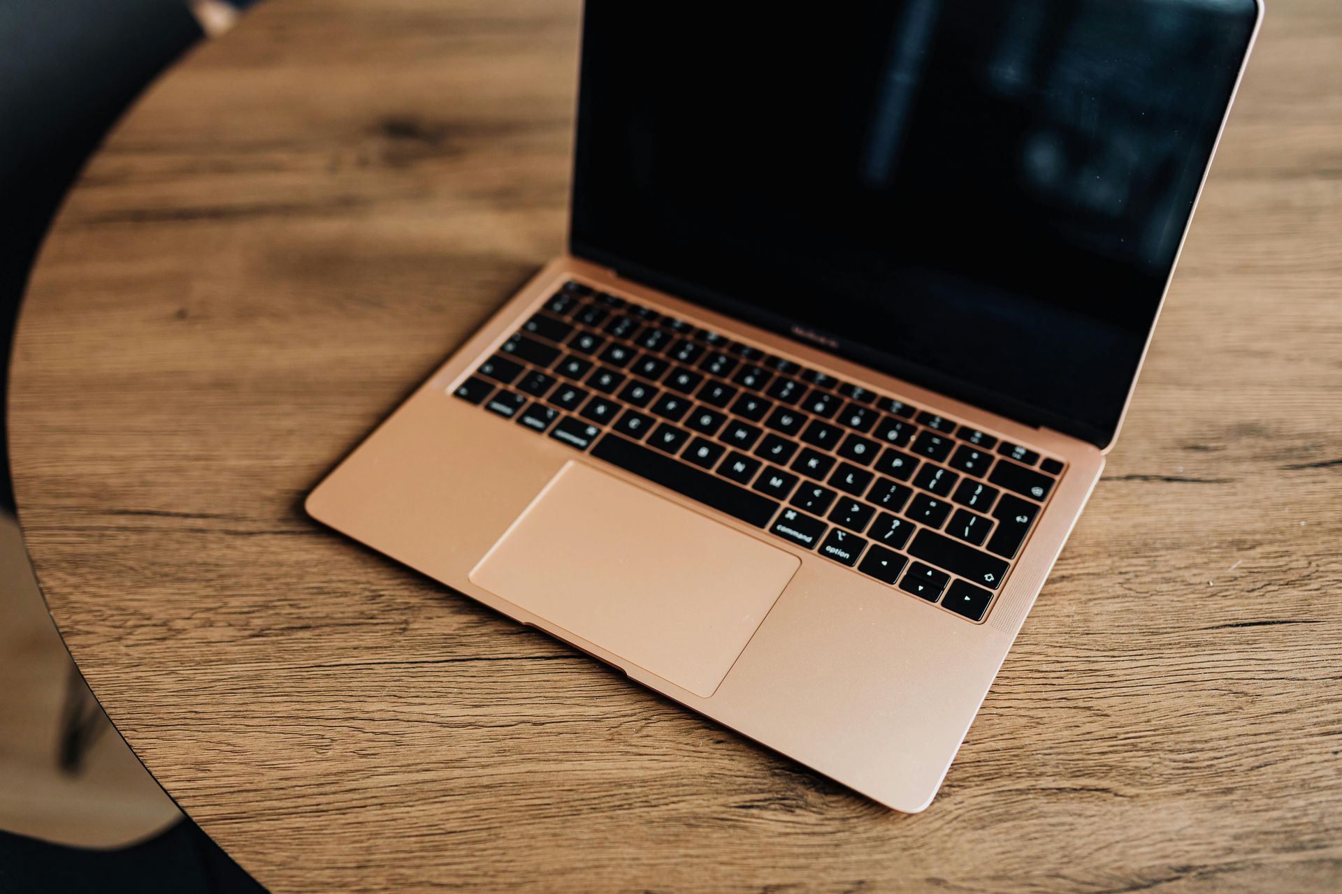 Open laptop on a wooden table, showing a black screen and pink keyboard.
