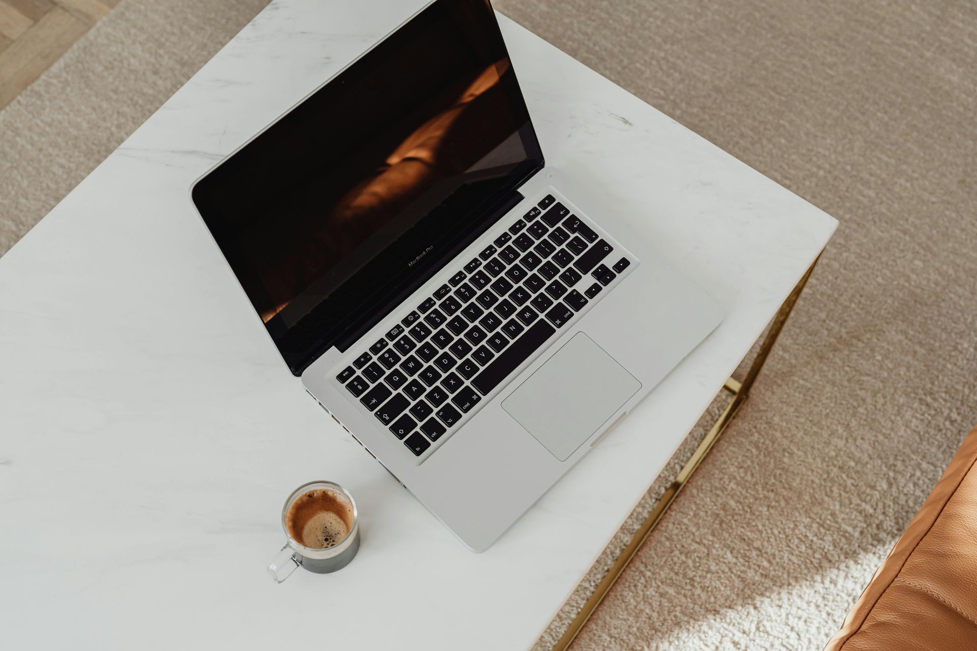 Laptop and coffee on a white table beside a tan sofa, viewed from above