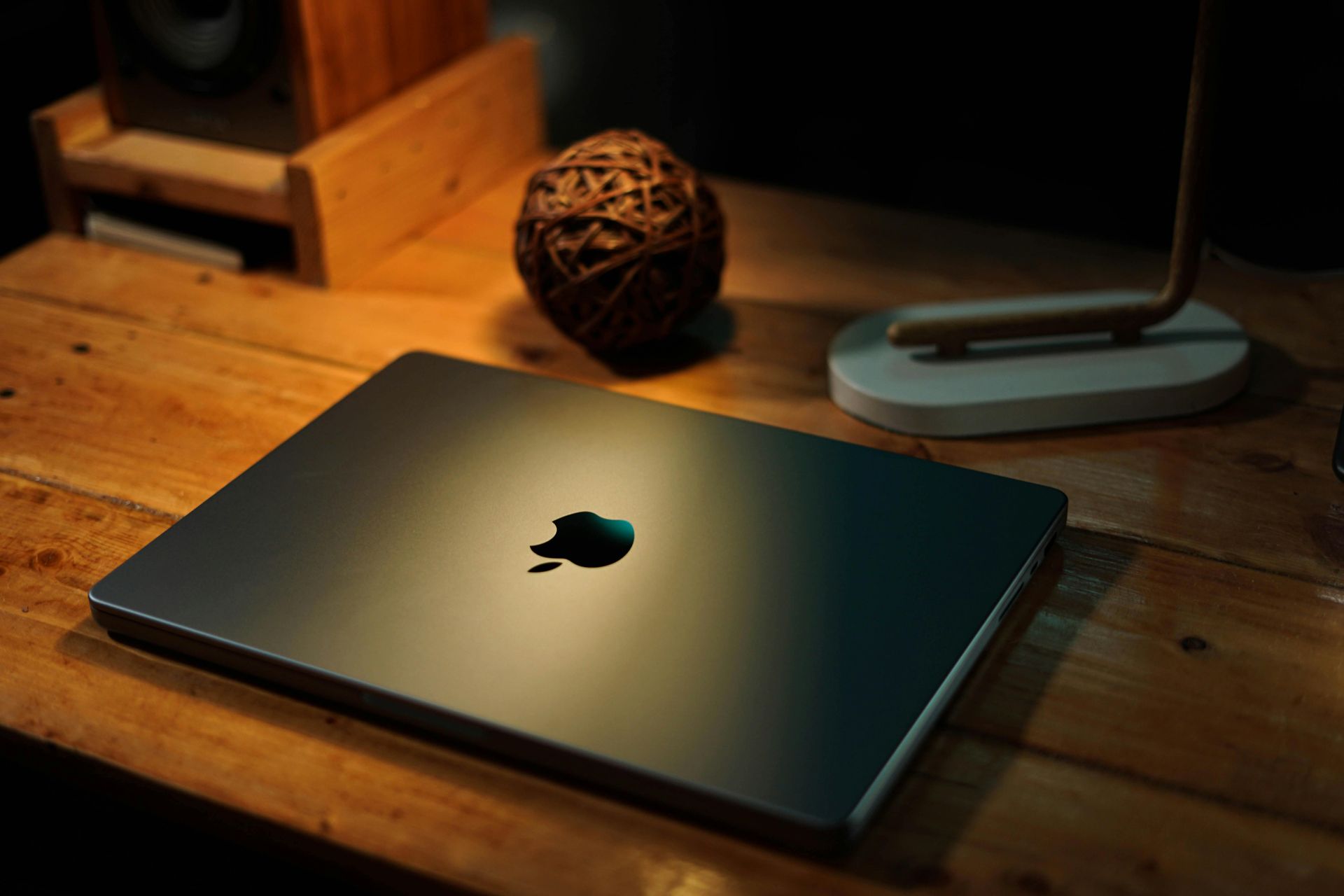 Closed silver laptop on a wooden desk beside a lamp and decorative ball.