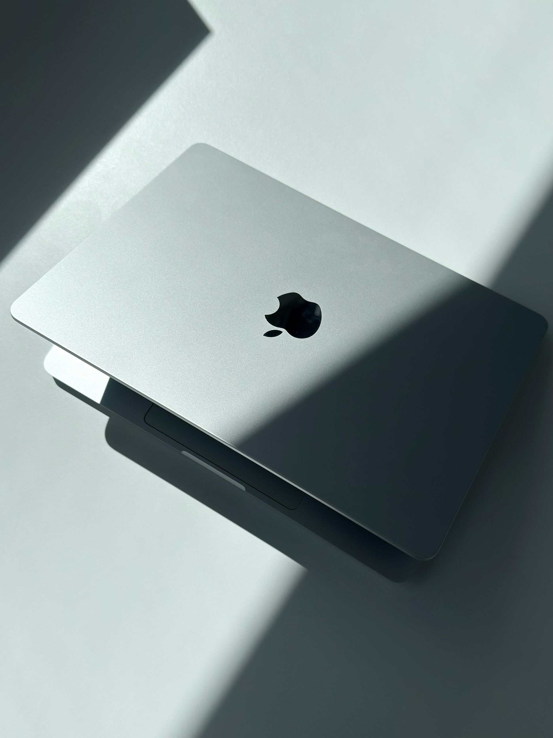 Closed silver MacBook on a sunlit surface with the Apple logo visible