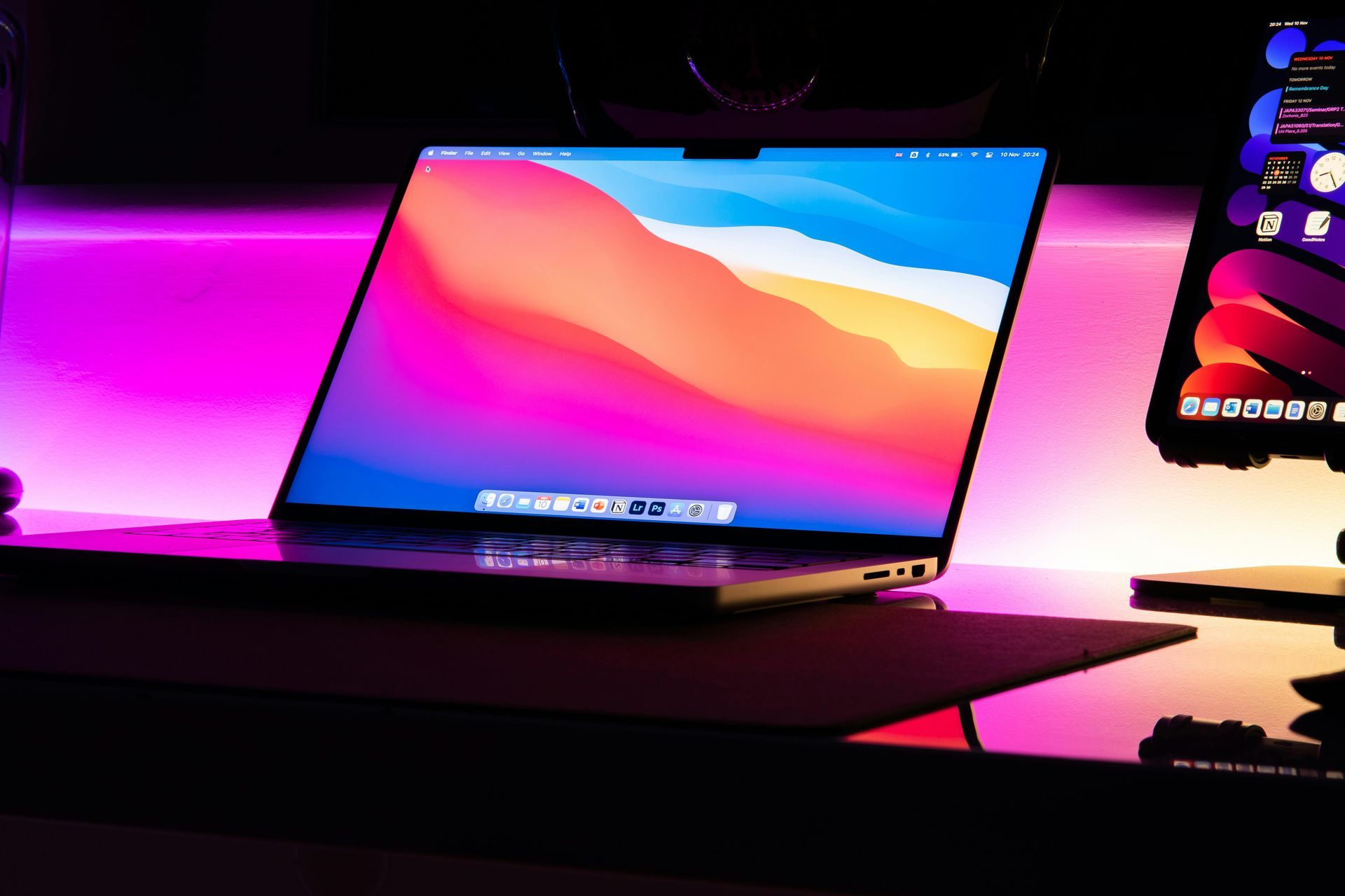 Laptop on a neon-lit desk displaying a colorful gradient wallpaper, with a smartphone beside it.