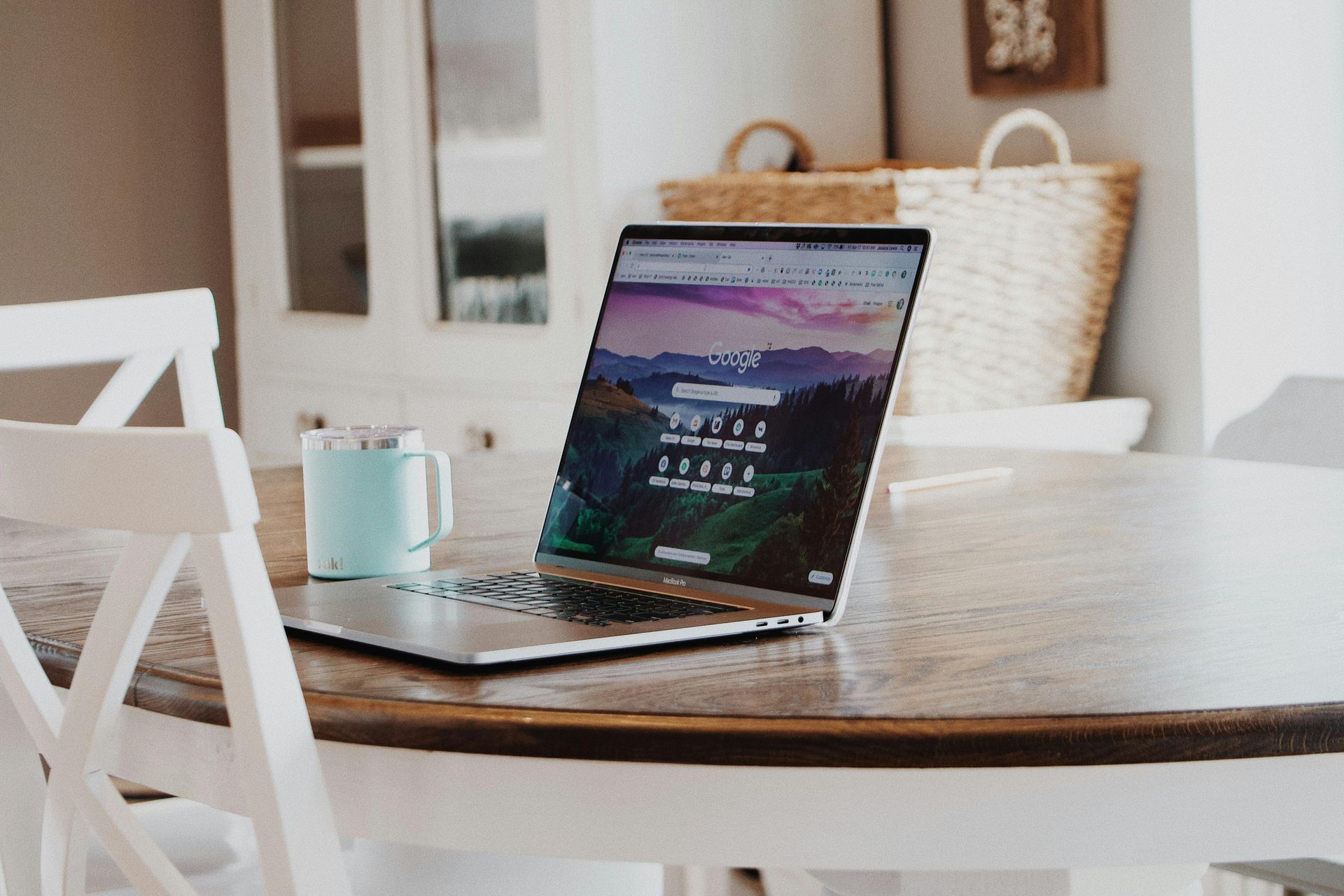 Laptop on a white table beside a teal mug in a bright kitchen nook