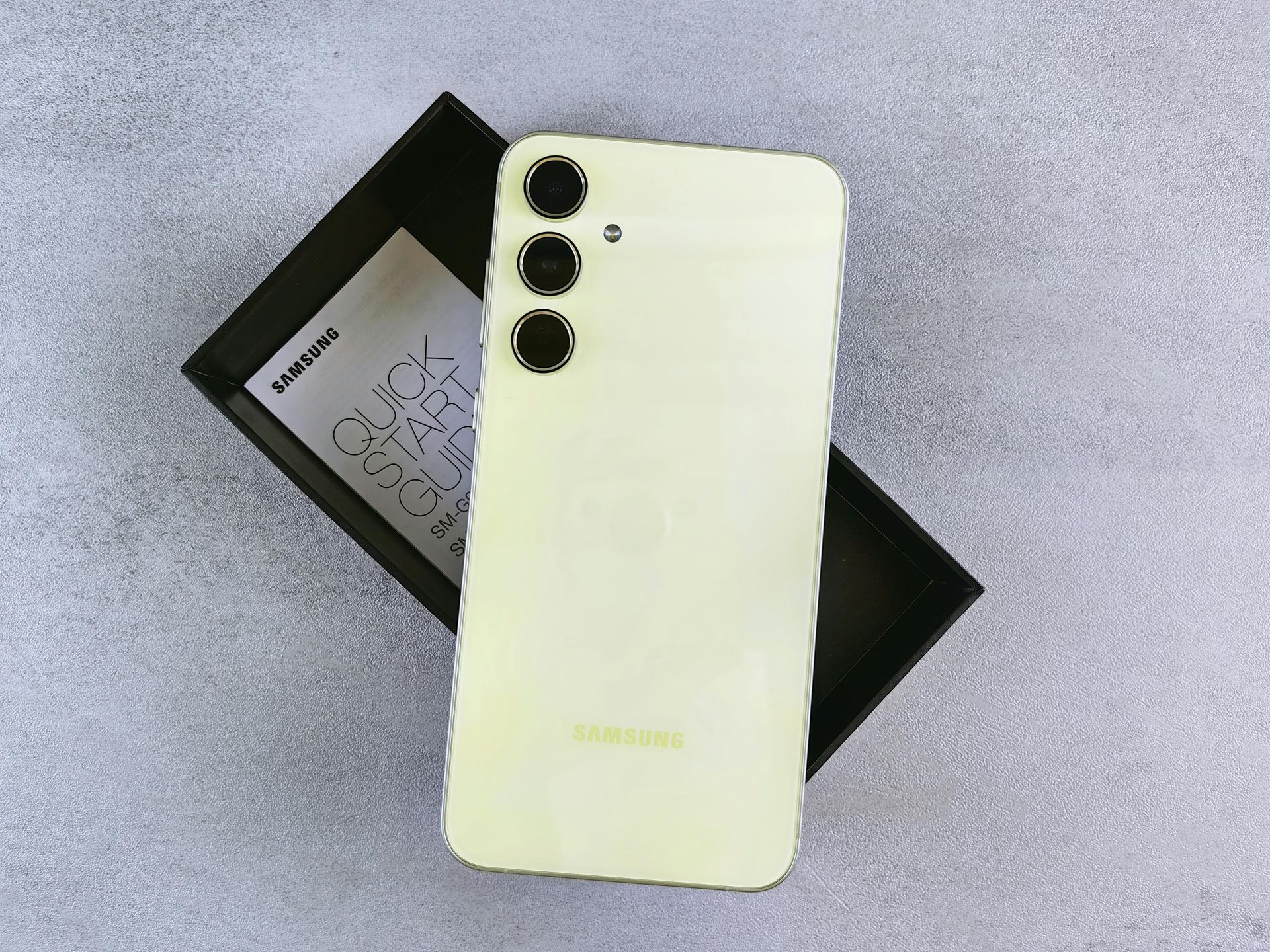 White smartphone with triple camera lenses resting on a black box on a light surface