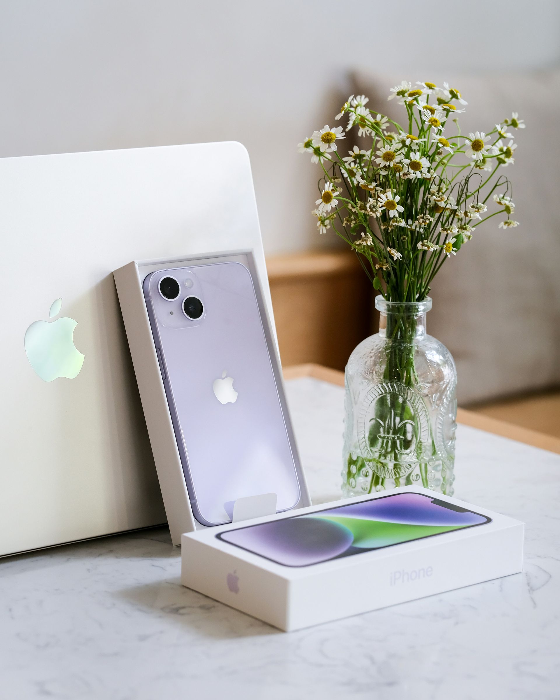 MacBook, iPhone, and flower vase on a white table