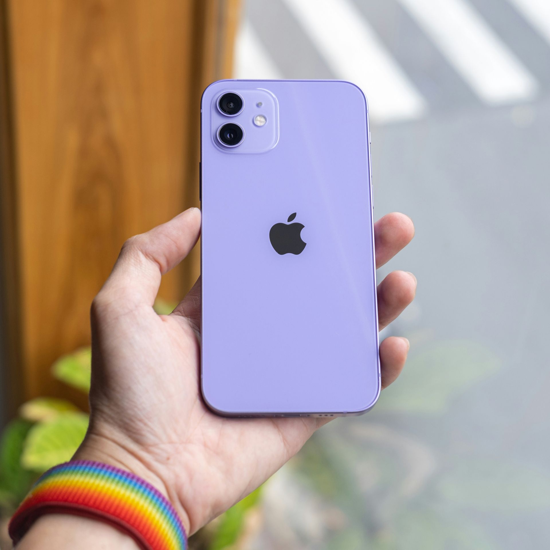 Hand holding a lavender iPhone with a black Apple logo near a window