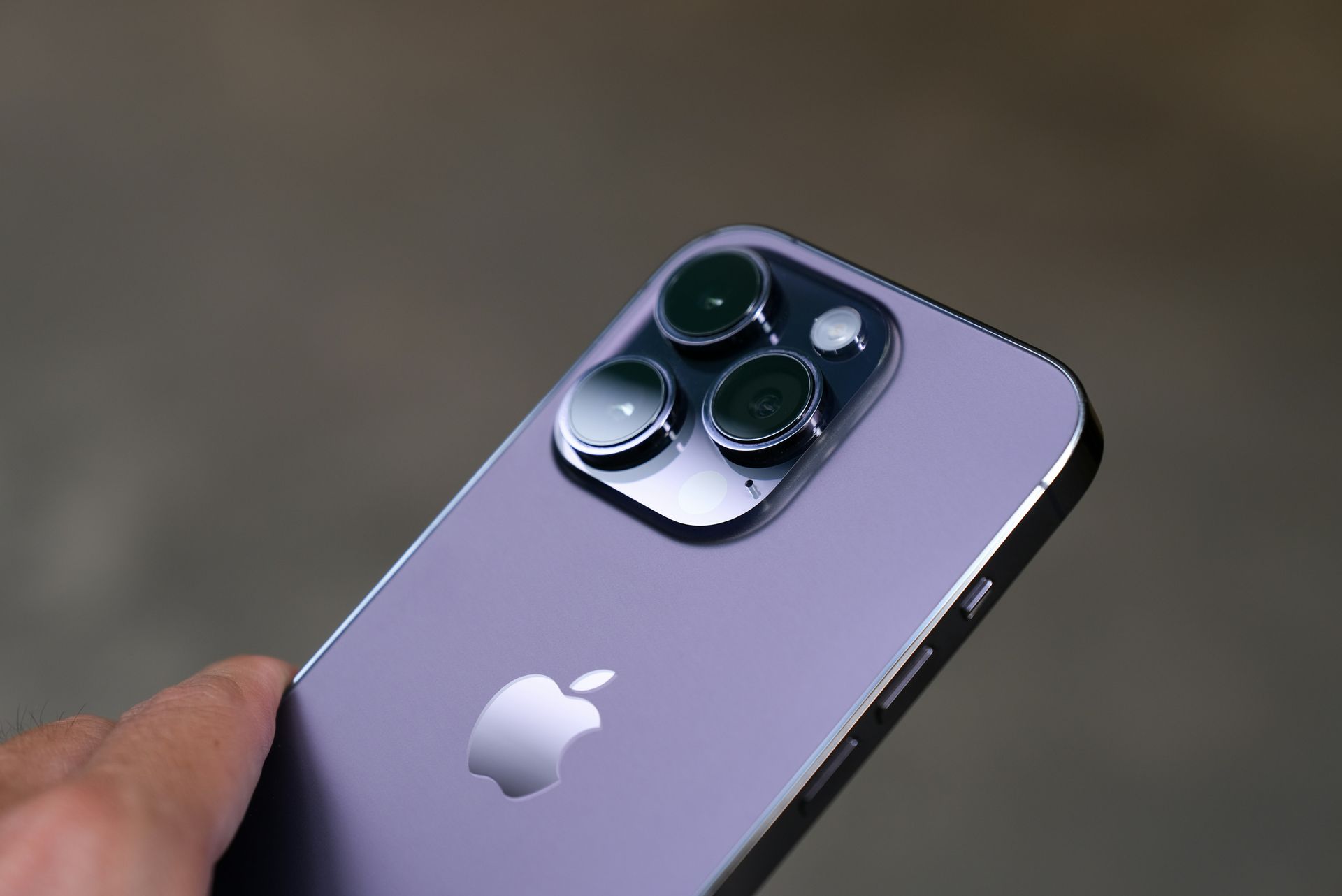 Hand holding a purple iPhone with triple rear cameras on a blurred background