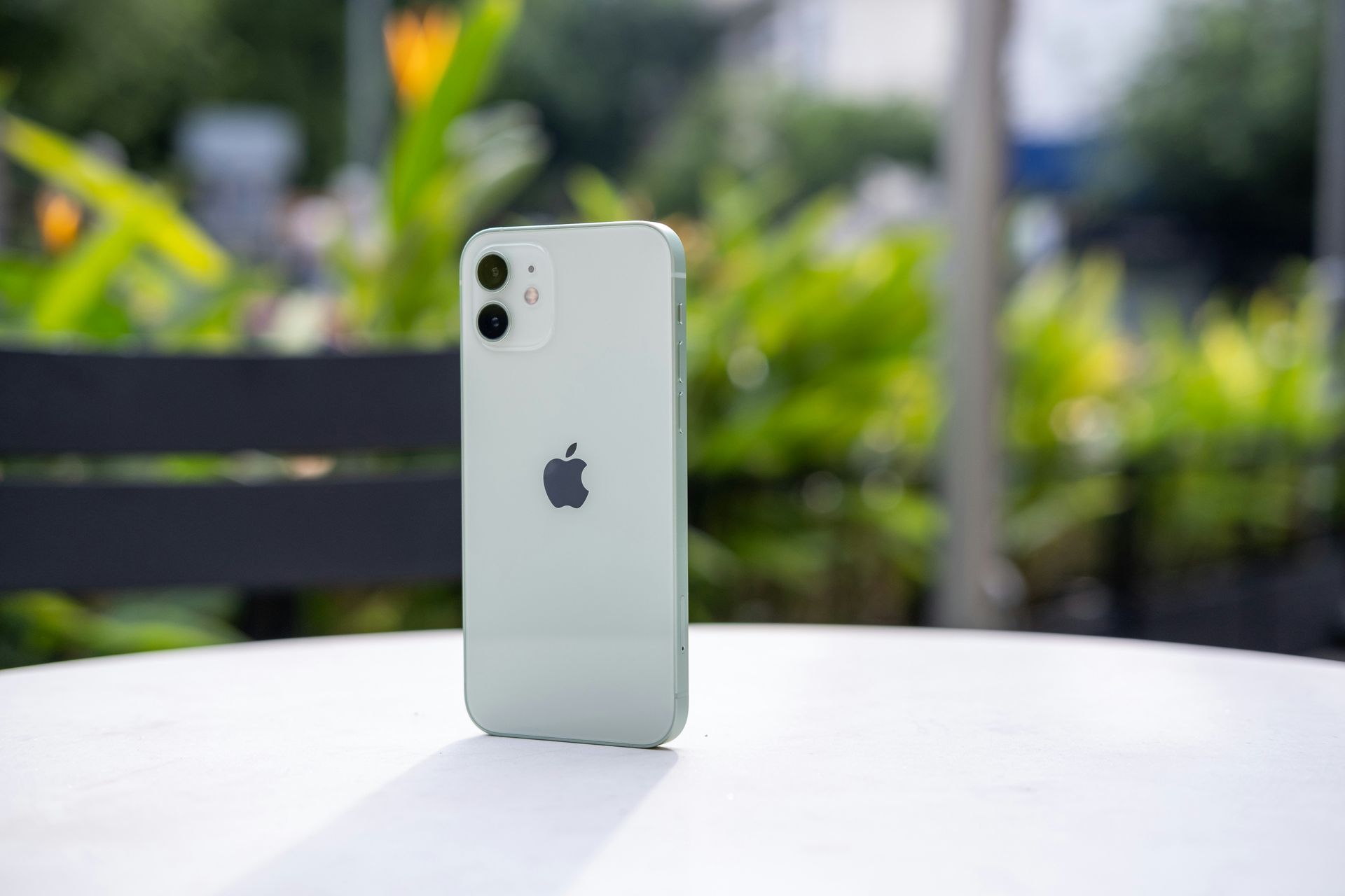 White iPhone standing on a table outdoors with blurred green plants in the background