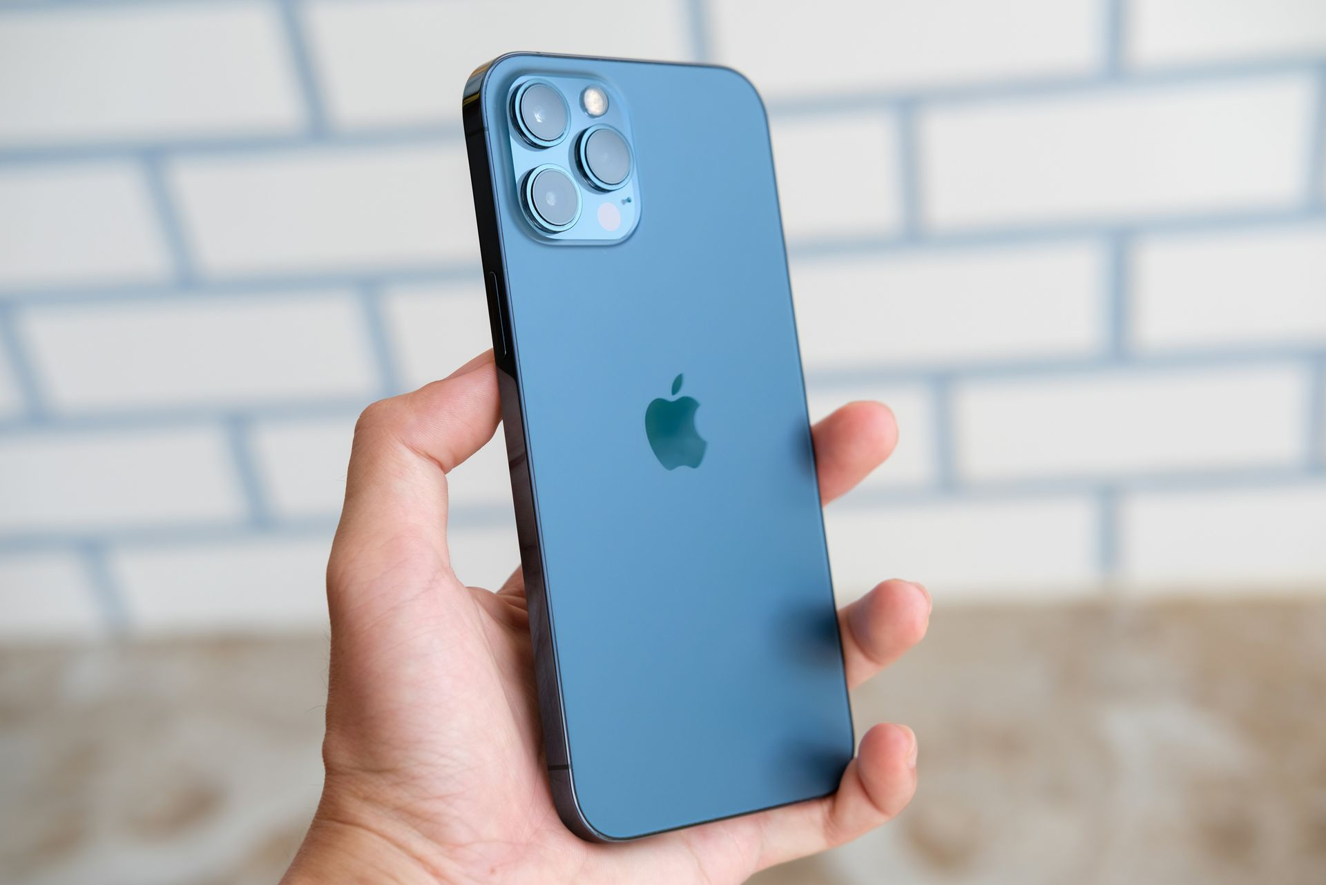 Hand holding a blue iPhone with triple camera against a blurred brick wall background