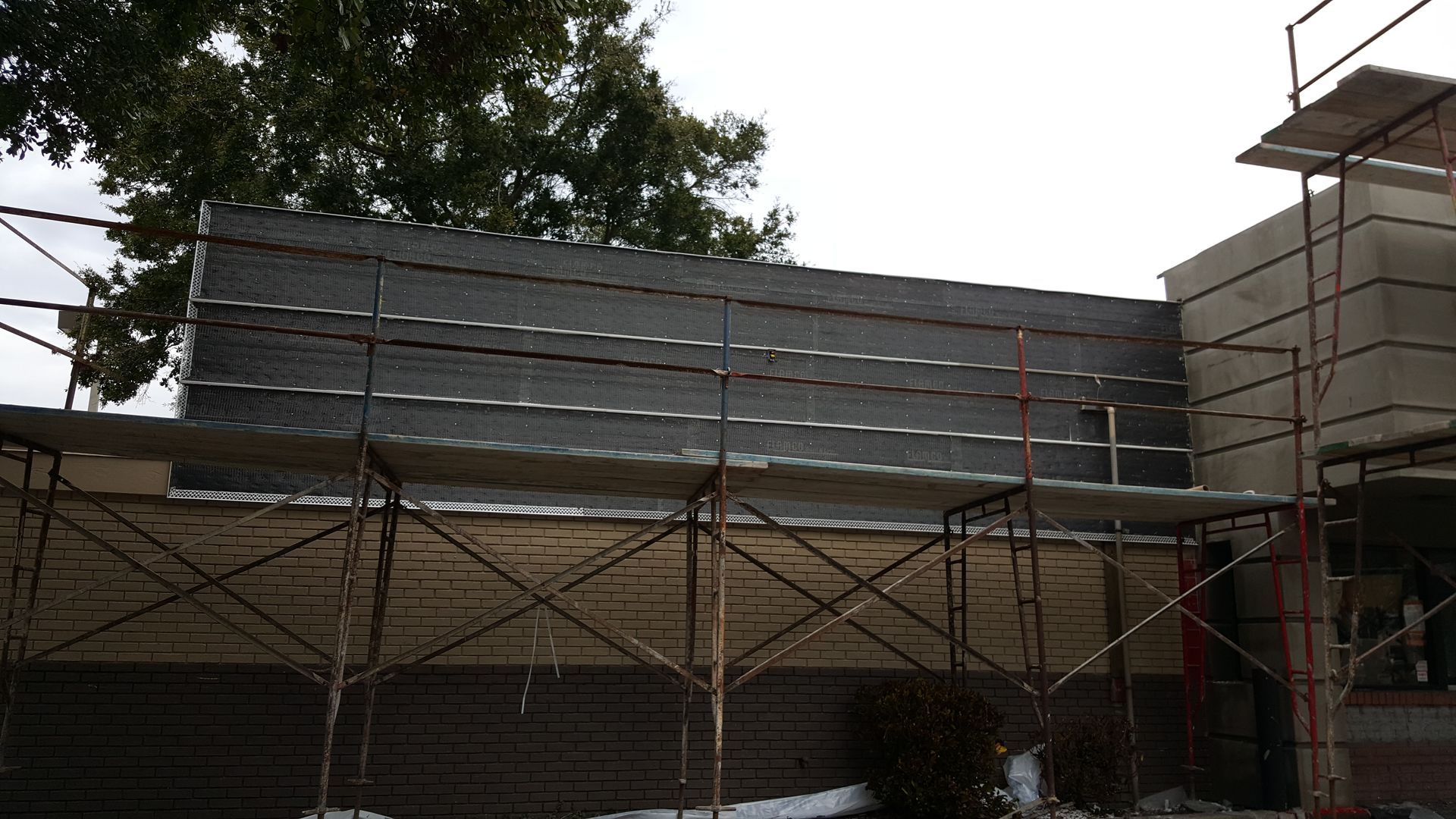 A building under construction with scaffolding and a tree in the background
