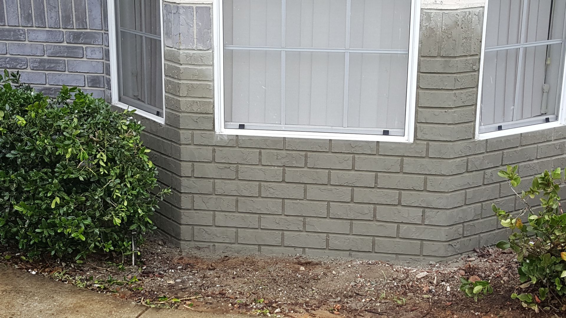 A brick building with a window and bushes in front of it.