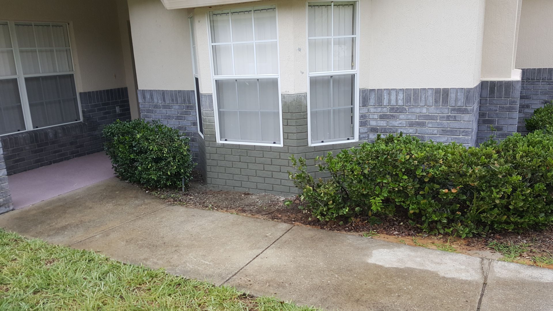 A house with a brick wall and a concrete sidewalk in front of it.