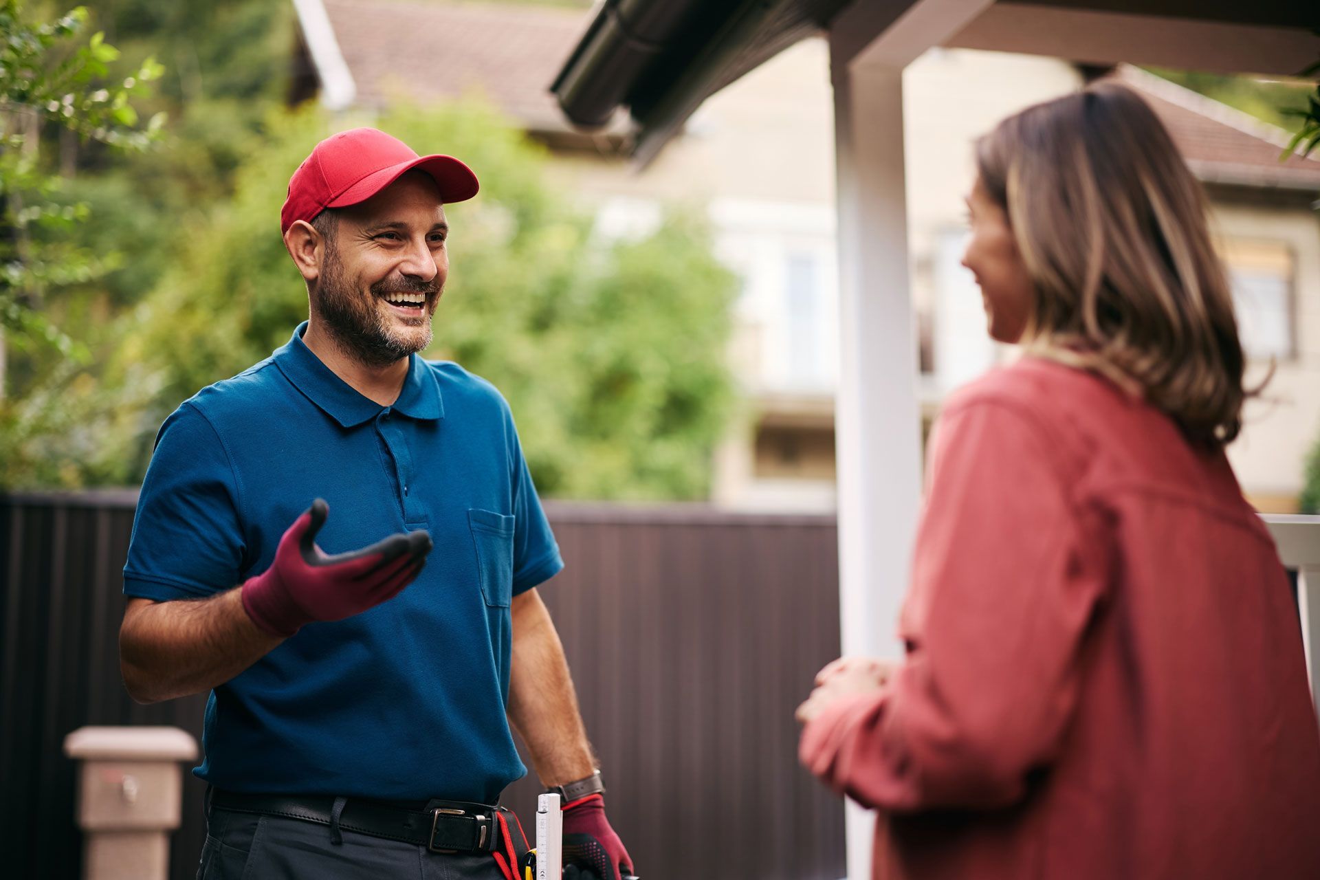 Two people talking outdoors, one in a red cap and blue shirt, the other in a rust jacket.