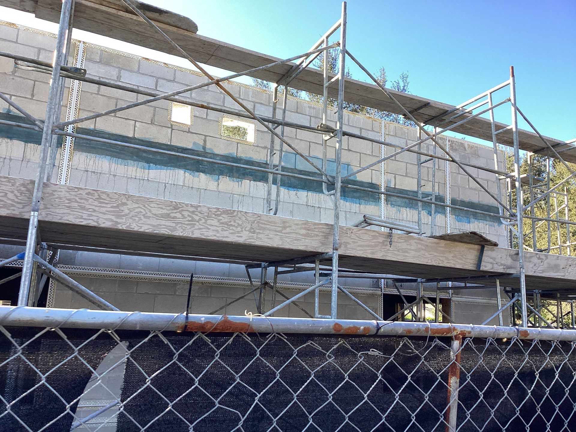 A chain link fence is surrounded by scaffolding on a building under construction.